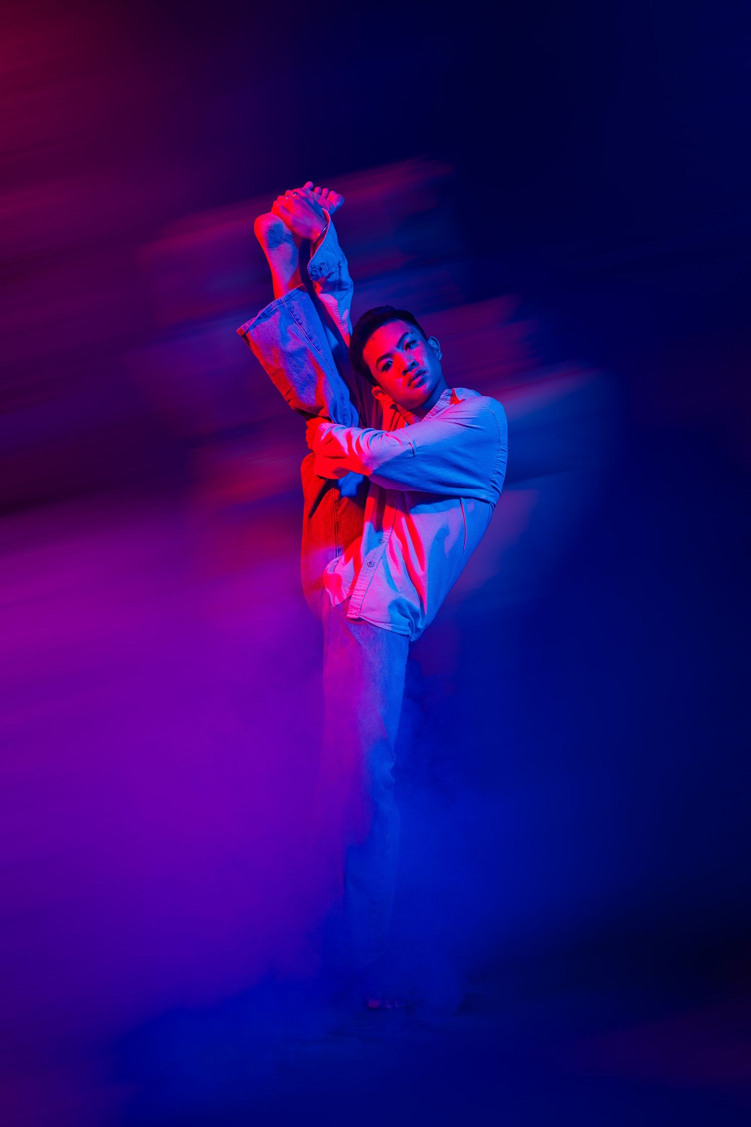 Dynamic dancer performs high kick in vibrant red and blue lighting creating dramatic motion blur effect.