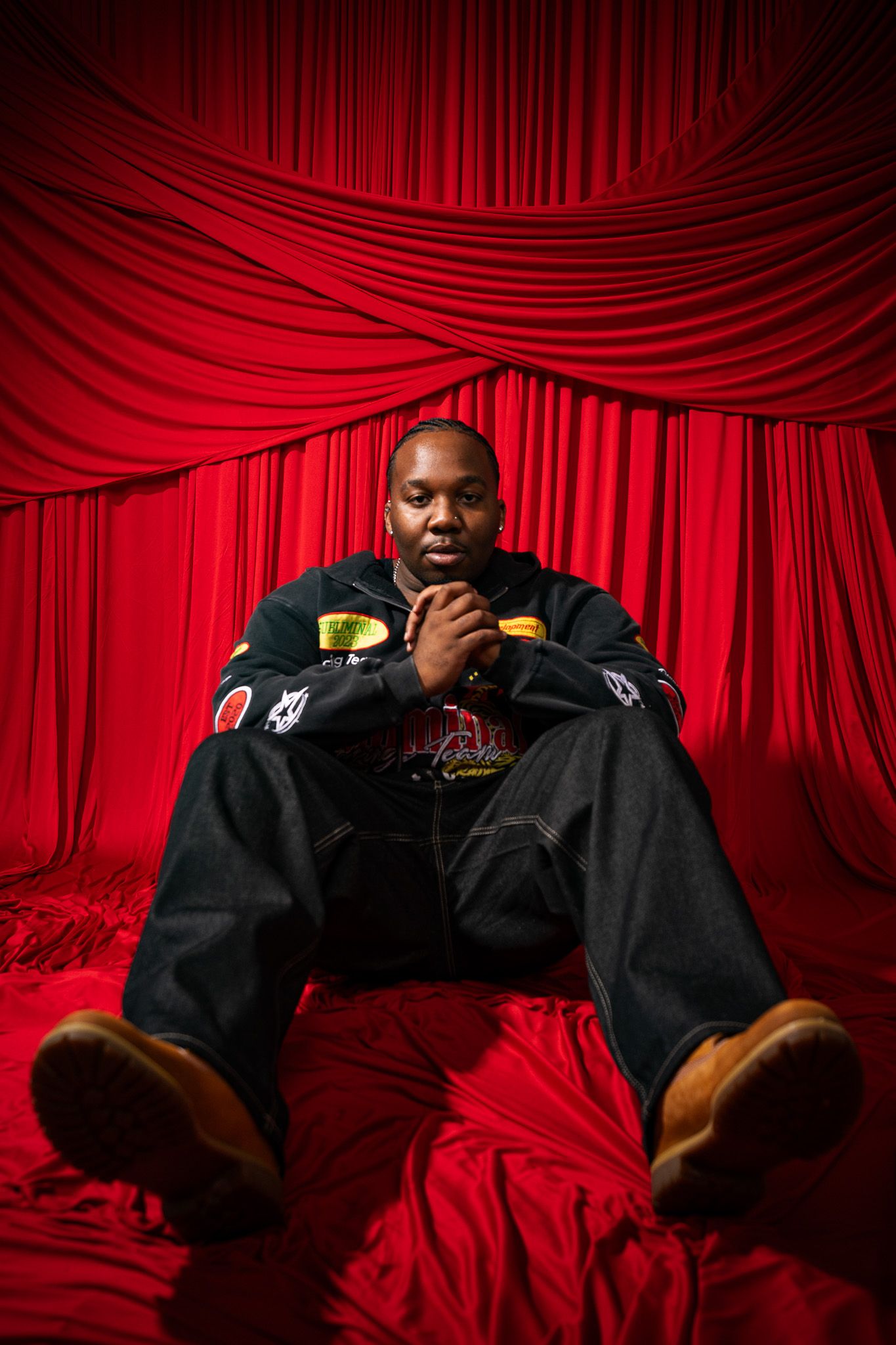 A person in black clothing rests on dramatic red velvet curtains in a portrait series taken from different angles.