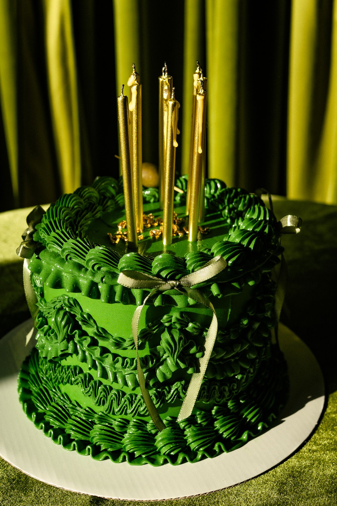 A detailed green fondant cake decorated with intricate ruffle patterns and golden candles on top.