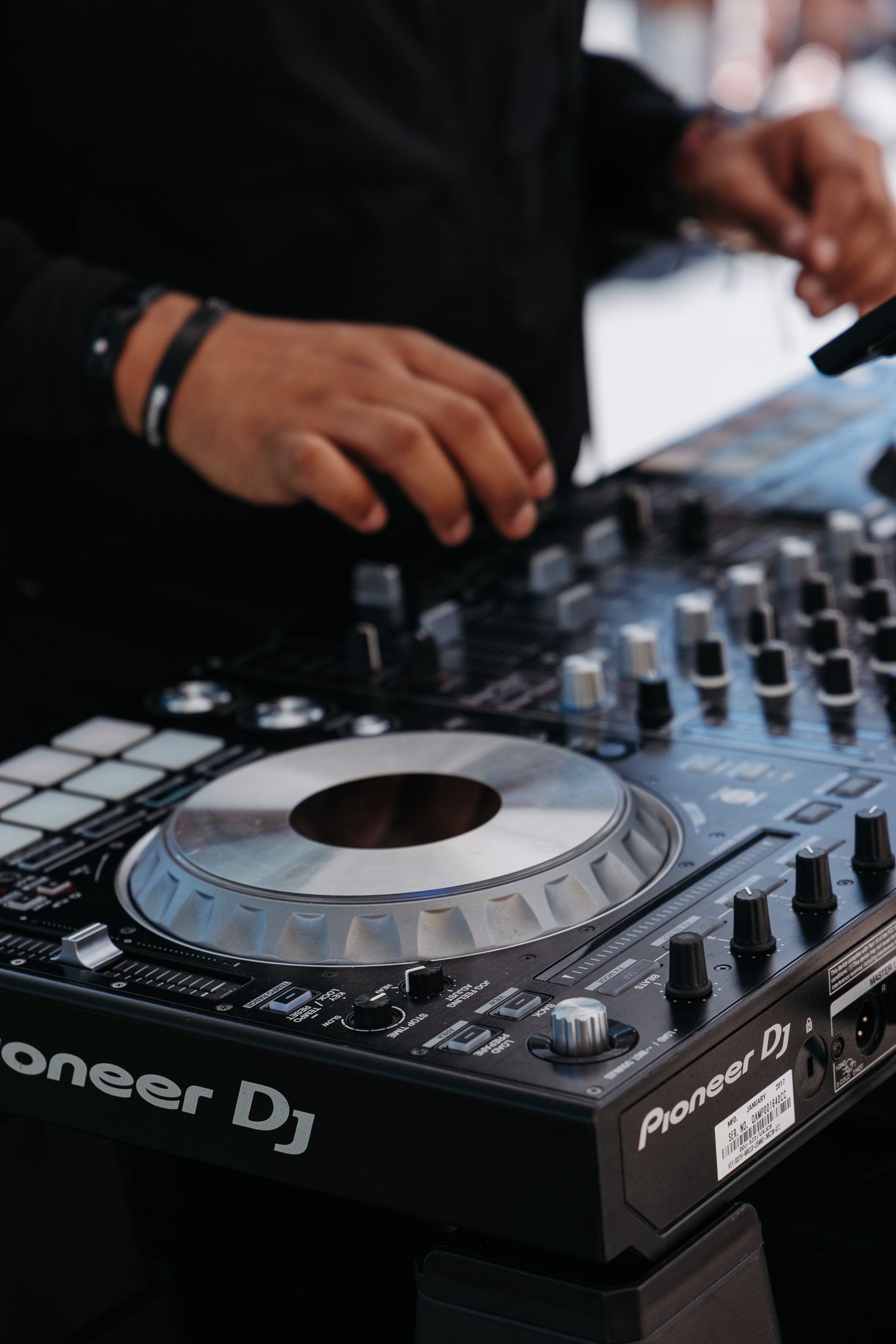 Close-up of hands operating a Pioneer DJ controller with knobs and buttons.