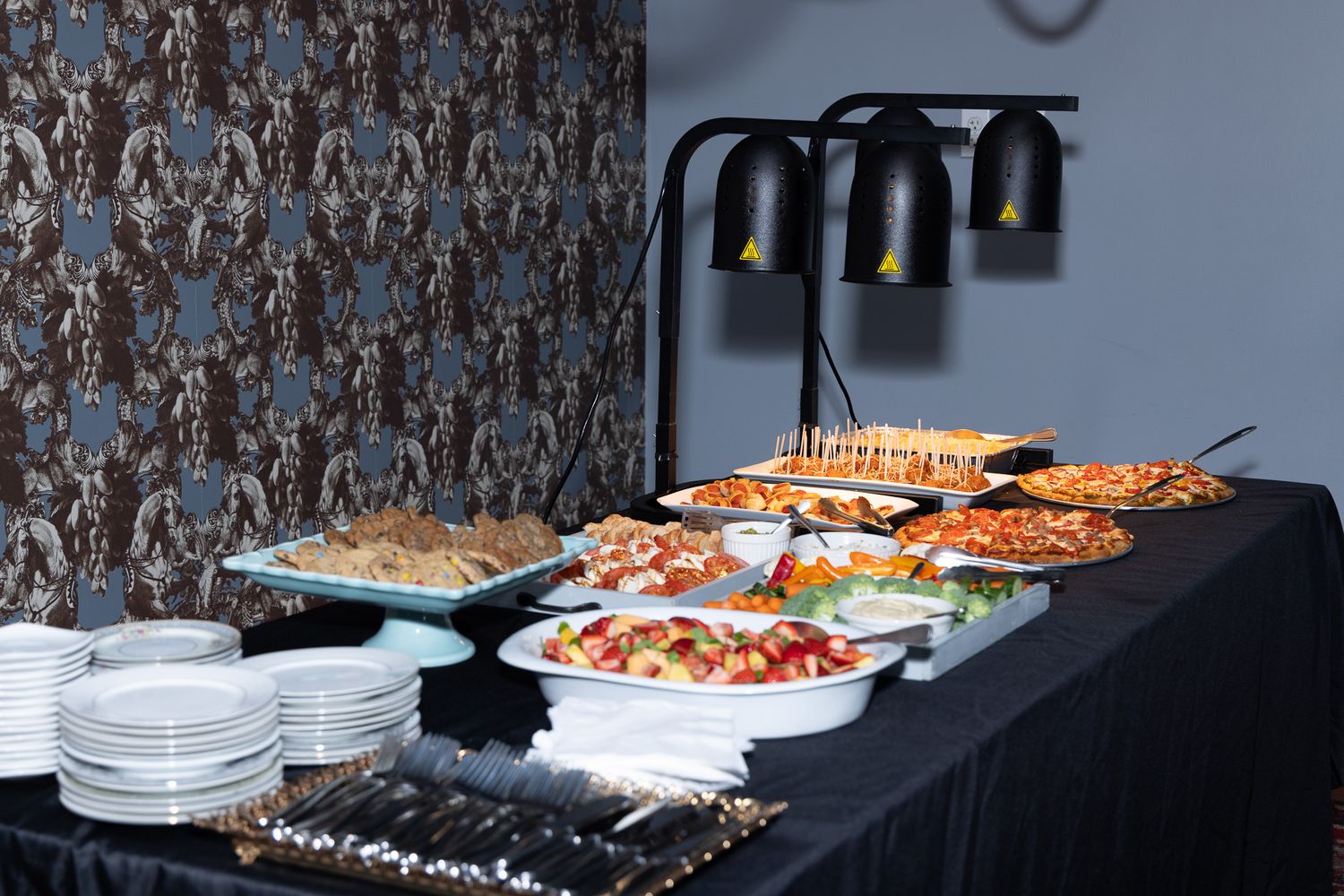 A buffet setup with heat lamps illuminating platters of seafood and appetizers on a dark tablecloth.
