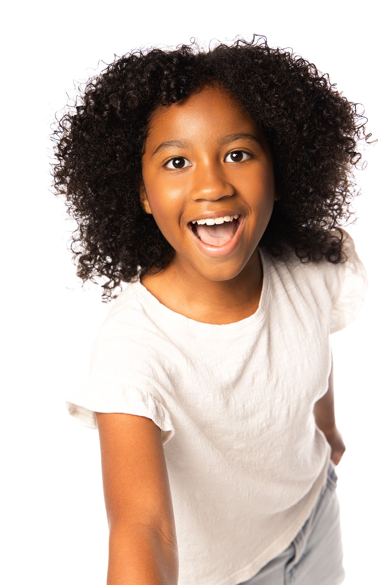 Child with natural curly hair wearing white t-shirt expressing happiness against white background.