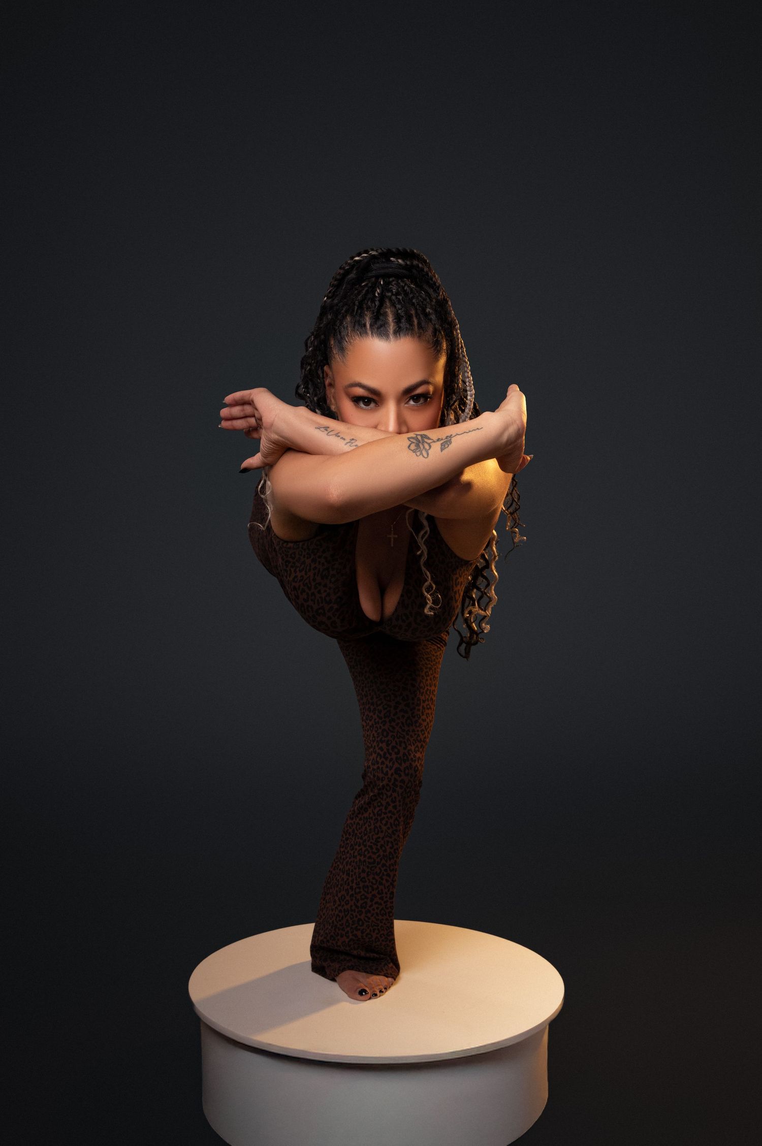 A dancer in a dark lace dress performs an artistic pose on a round white platform against a black background.