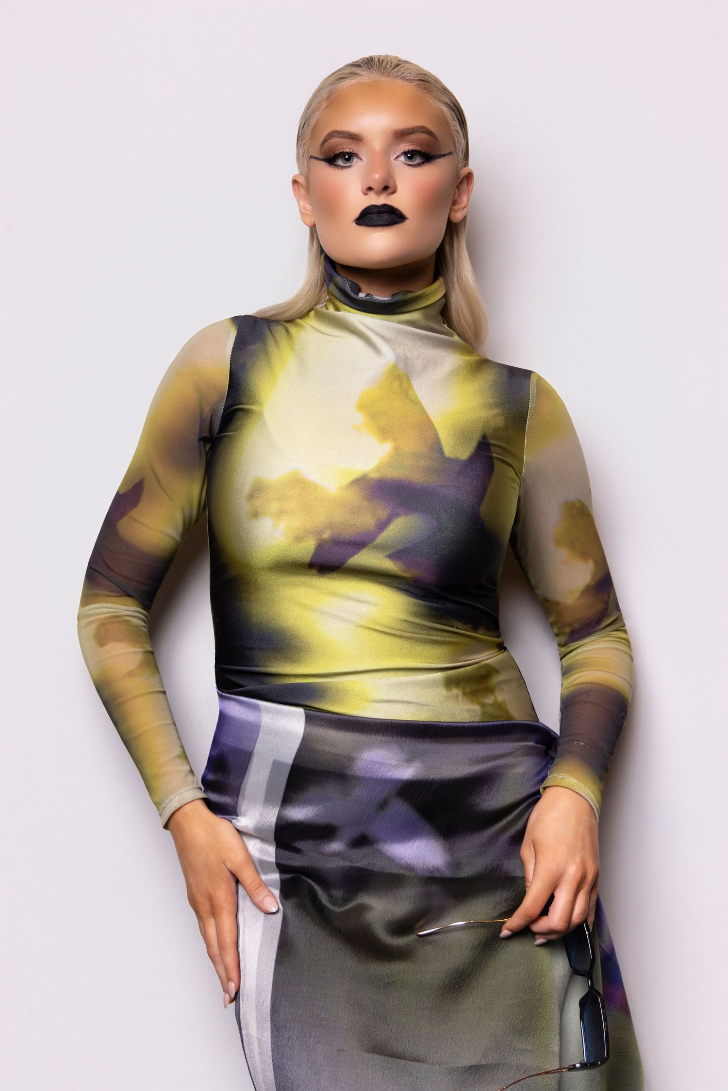 Fashion model wearing yellow and gray tie-dye top with dramatic dark lipstick in studio photoshoot series.