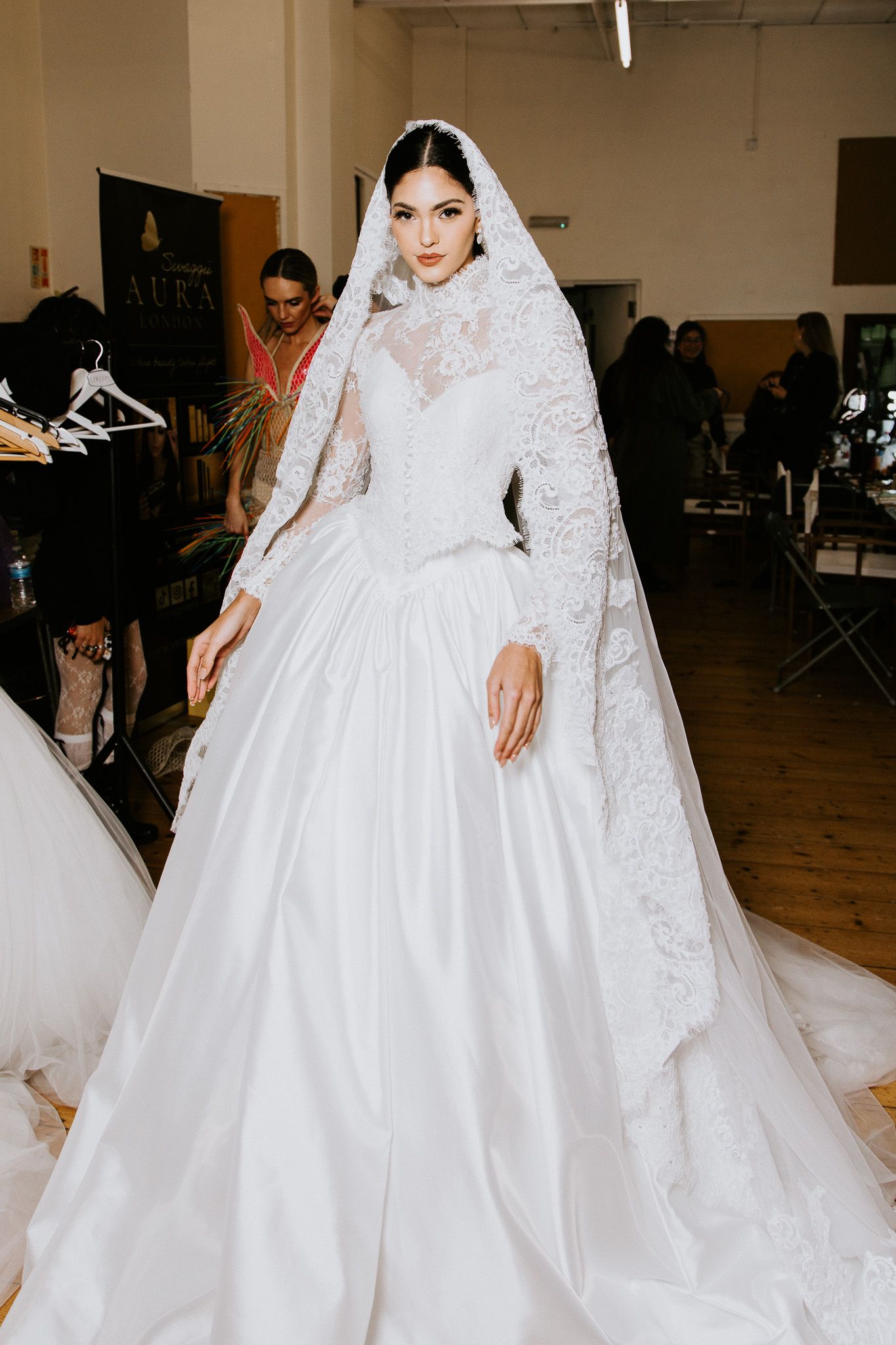 Behind-the-scenes bridal fitting showing intricate details of white lace wedding gown with cathedral veil.