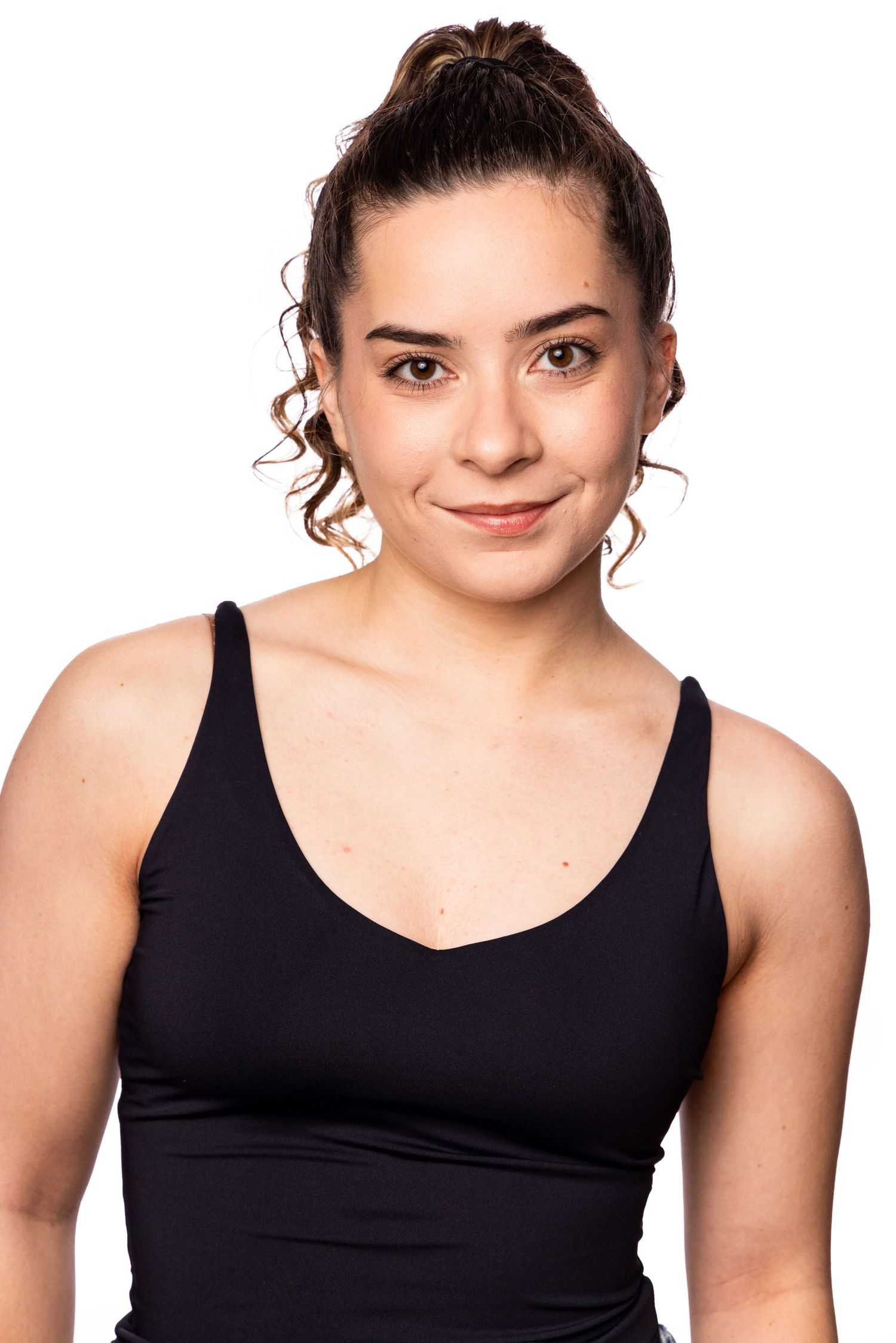 A person with curly hair in a bun wearing a black tank top poses against a white background.