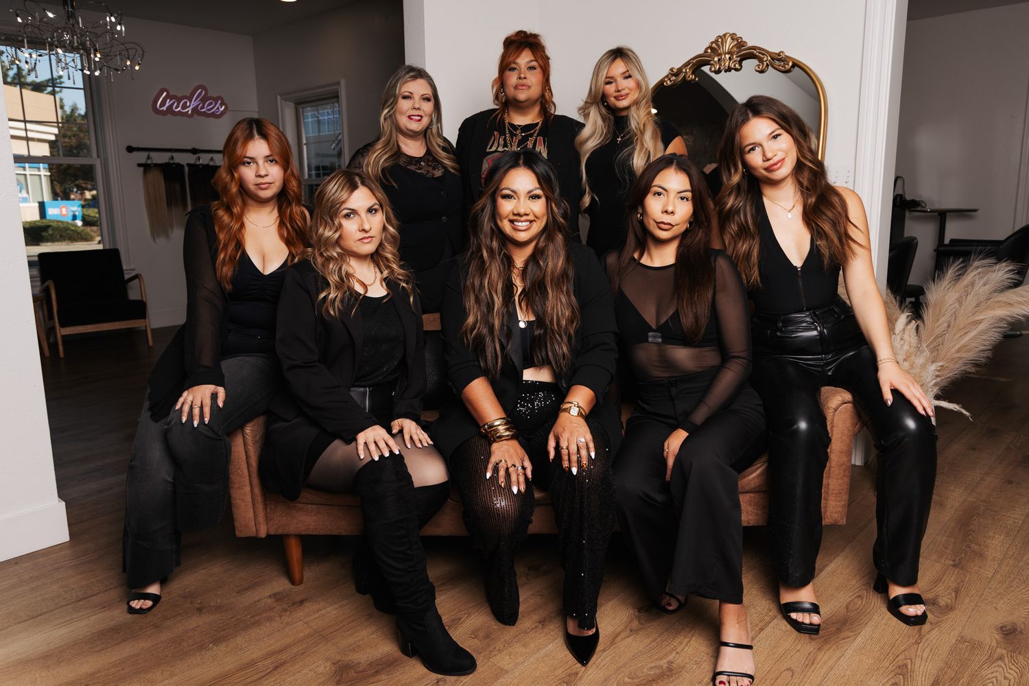 A group in coordinated black outfits poses together on a couch in a modern interior space.