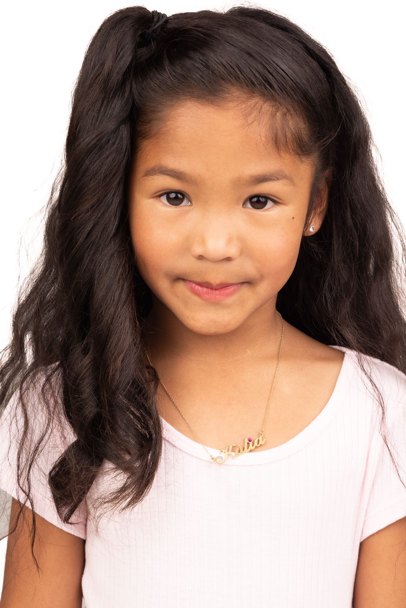 A sequence of cheerful expressions from a child with long dark hair wearing a pink top against white background.