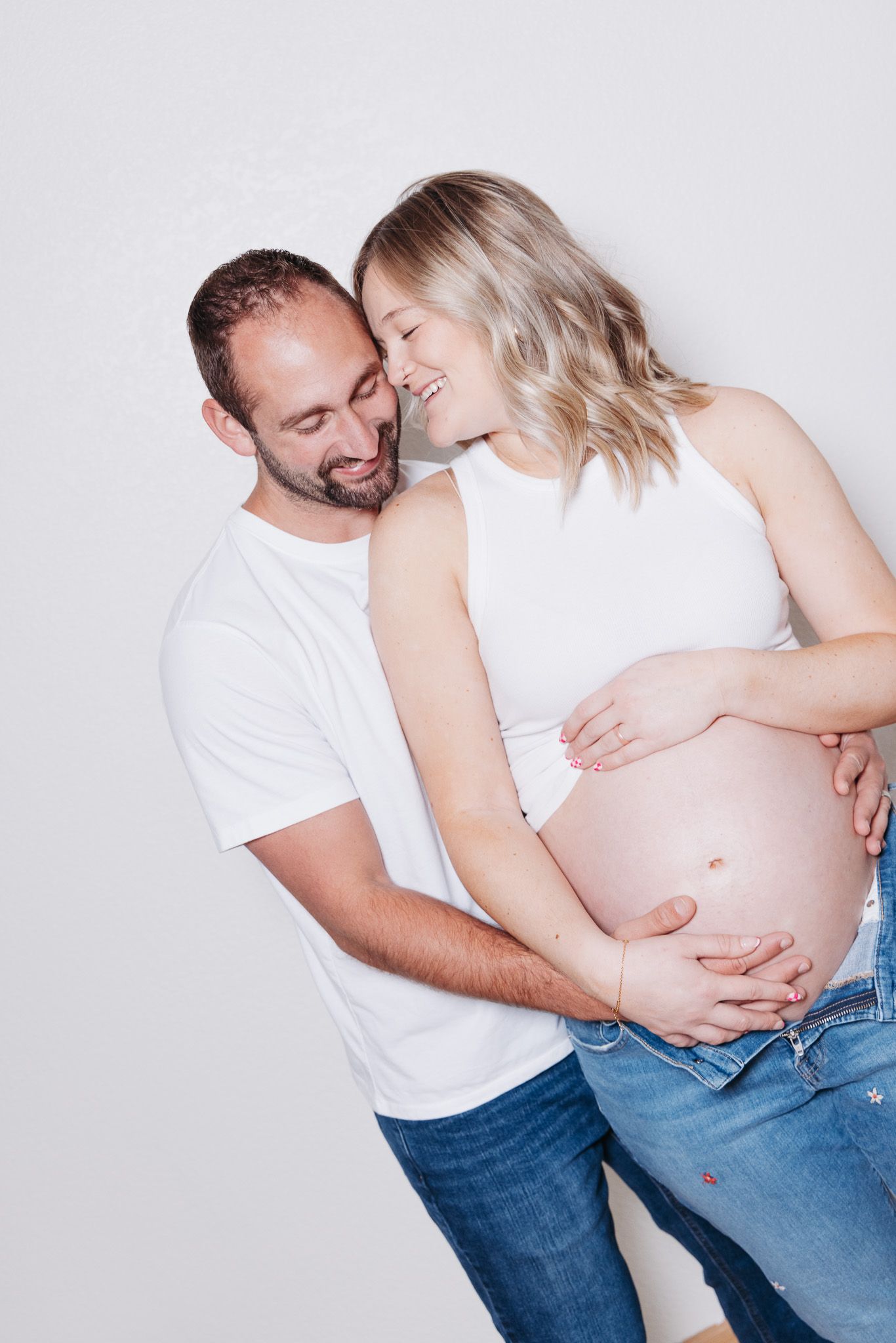 A loving couple embraces while showing off a pregnant belly in a series of intimate maternity photos.