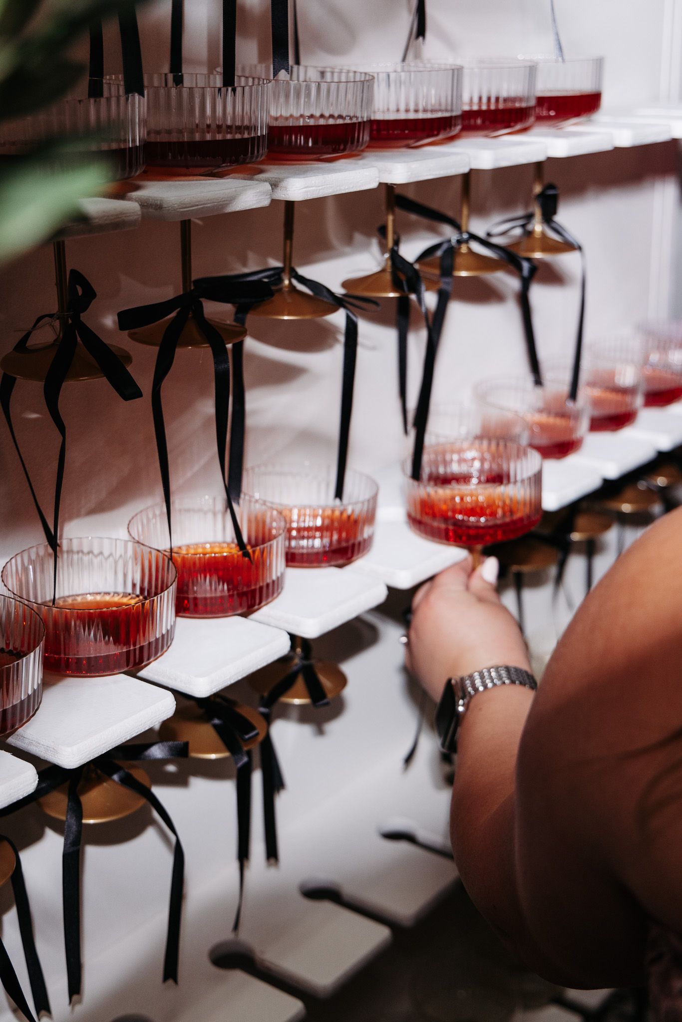 Rows of red cocktails in clear glasses hanging from black holders on a white display wall.