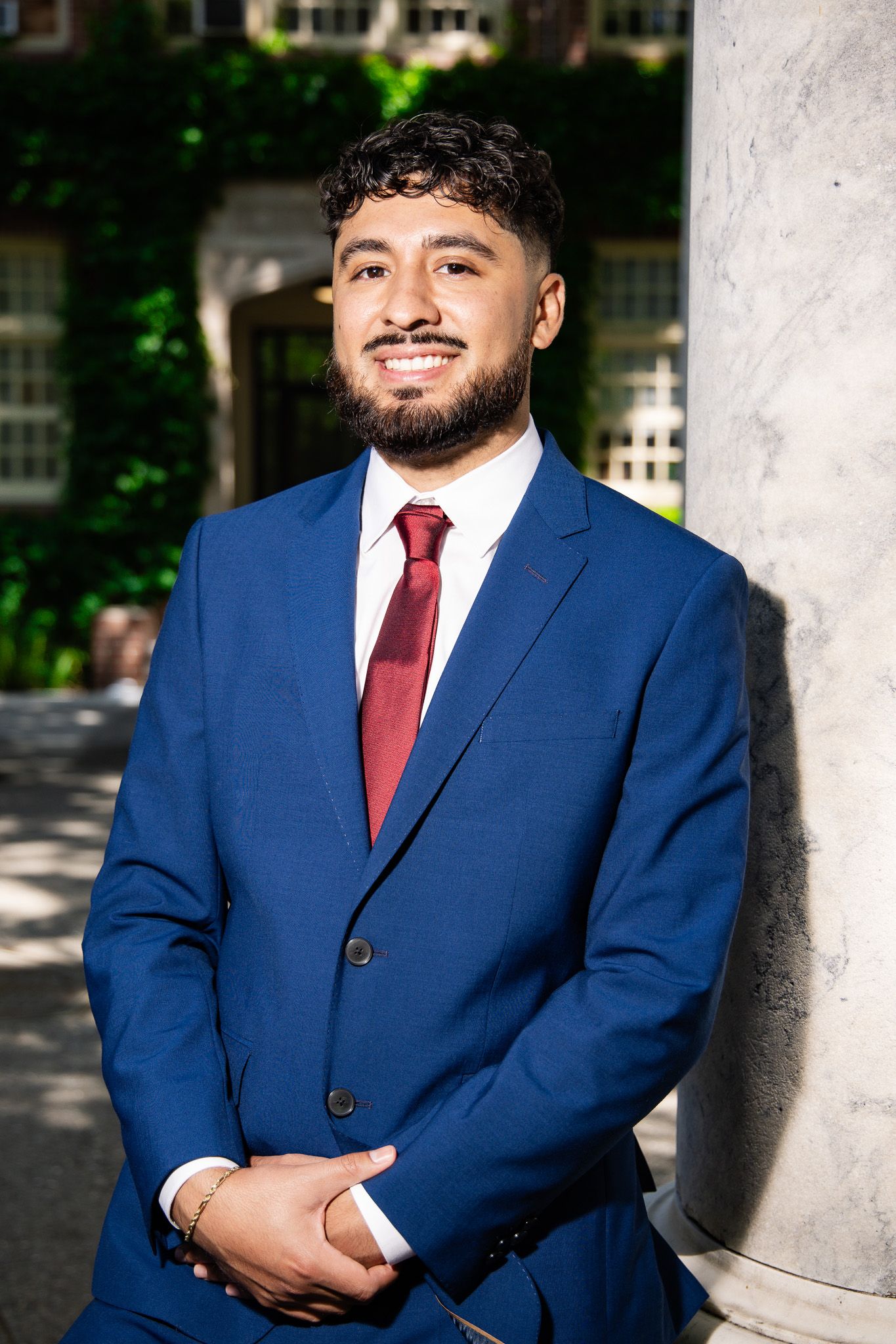 A series of professional headshots showing someone in a navy blue suit with a burgundy tie against a light architectural backdrop.