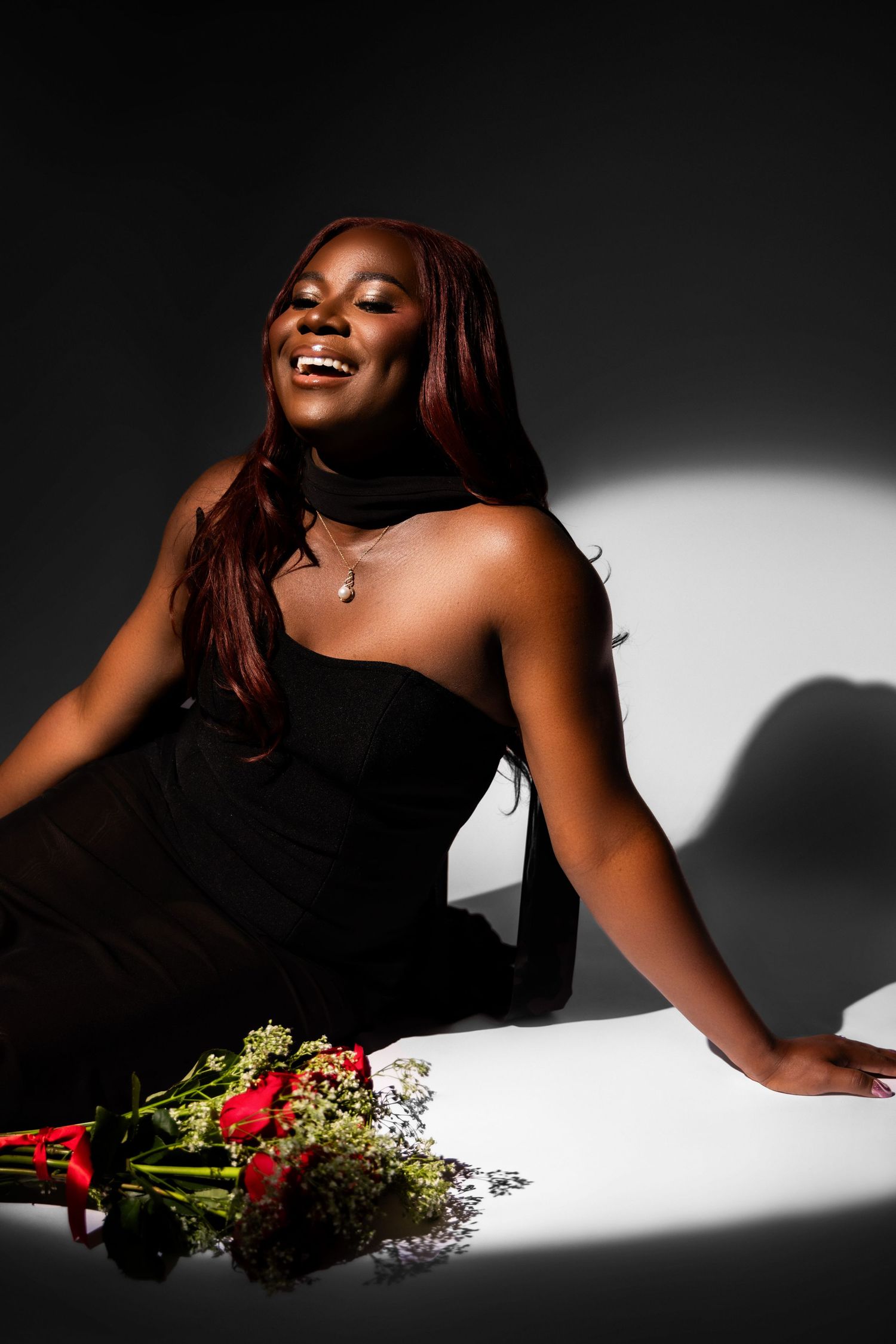 Dramatic studio portrait with black dress and red roses creating striking contrast in black and white lighting.