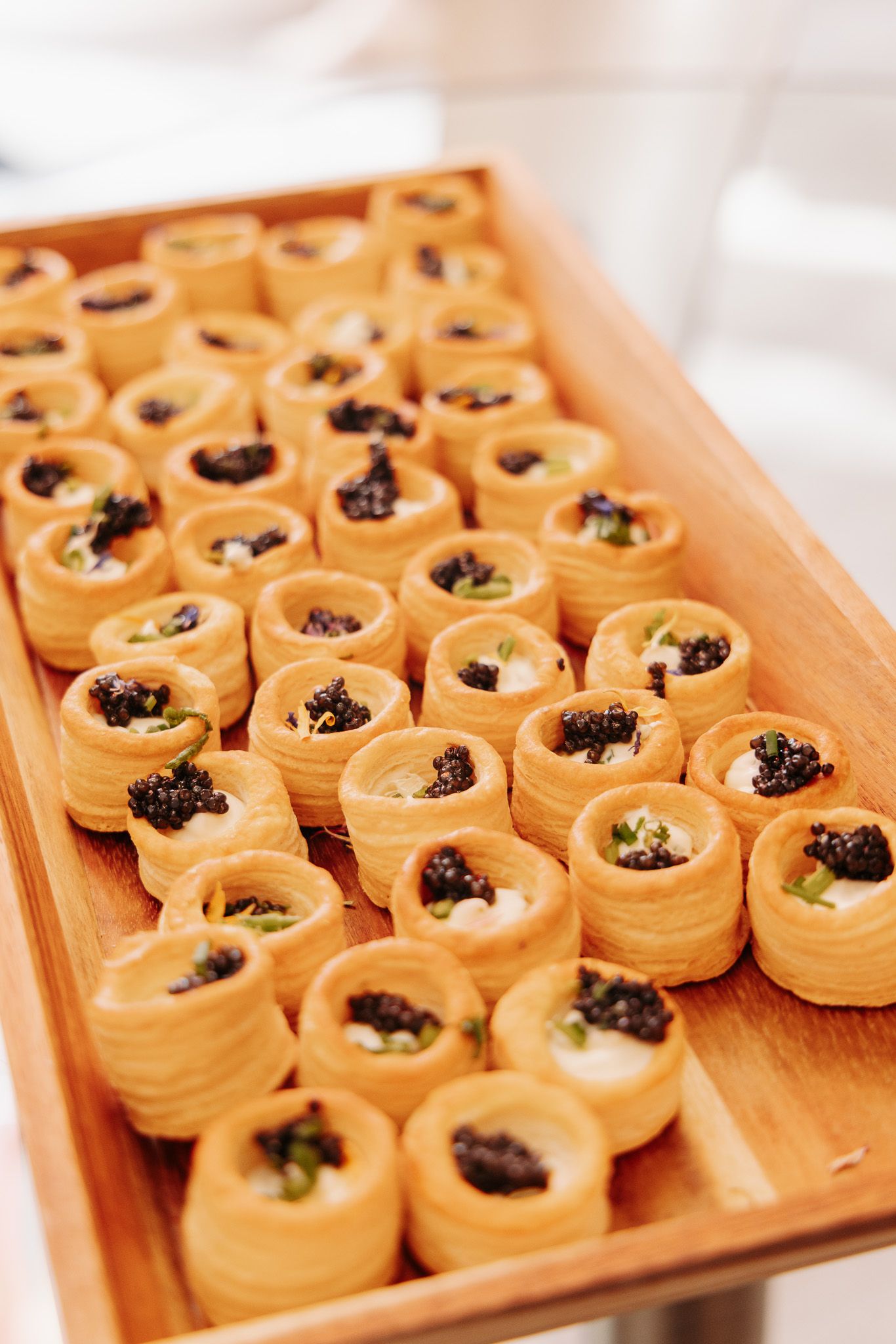 Fresh salmon and caviar appetizers arranged in rows on a wooden serving board at a catering event.