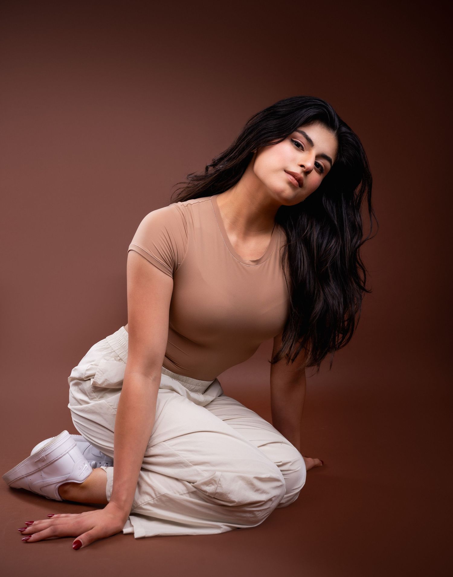 A figure in a beige bodysuit and white fabric creates an artistic pose sequence against a dark brown backdrop.