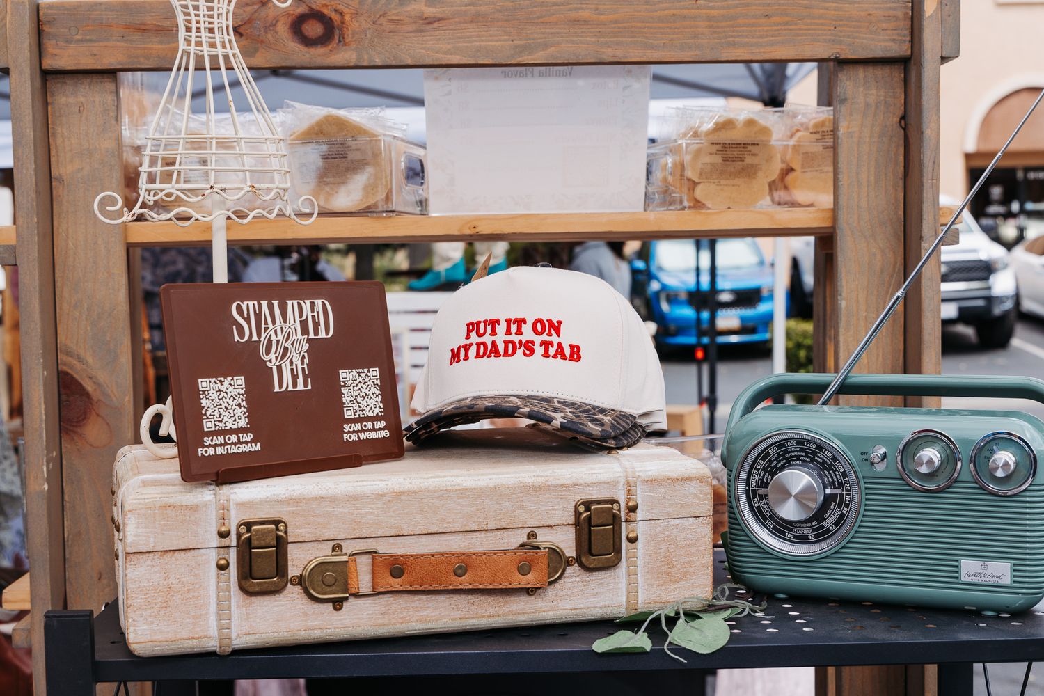 Vintage suitcase display with a white trucker hat reading Put It On My Dads Tab and a retro green radio at a market.