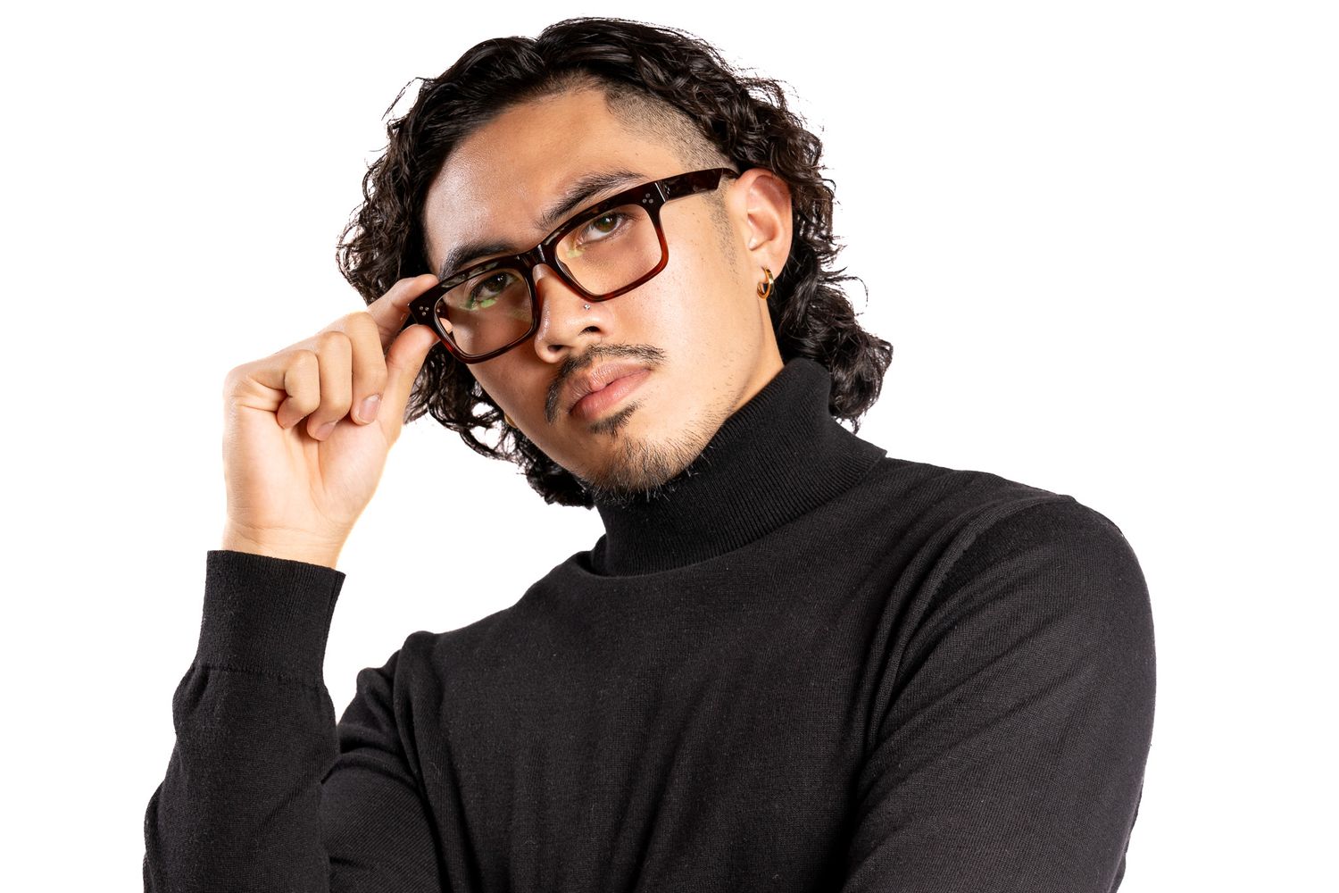Thoughtful Asian man with curly hair touching glasses, wearing black turtleneck on white background.