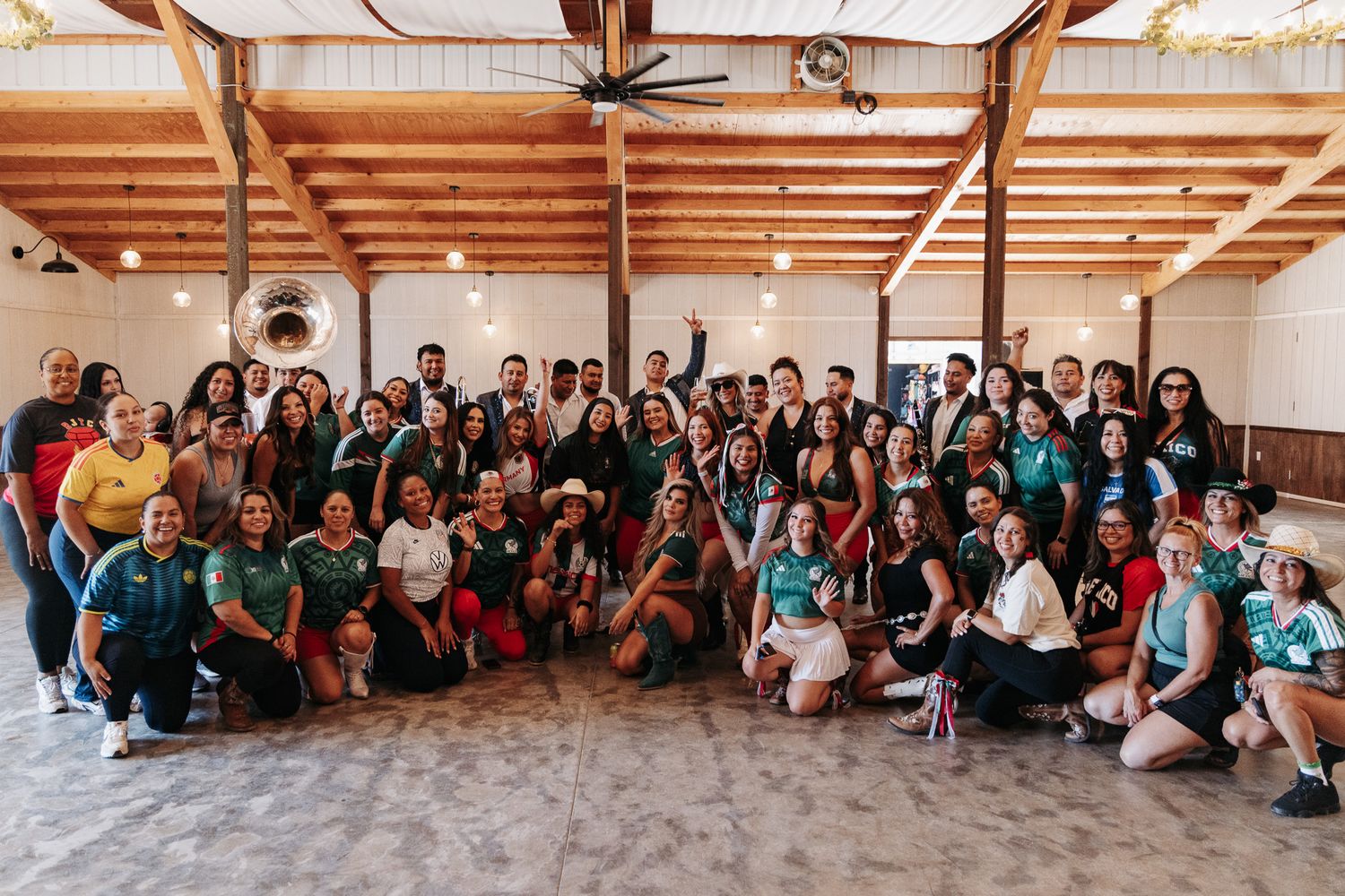 Large group of people posing together indoors under wooden beam ceiling, many wearing green sports jerseys.