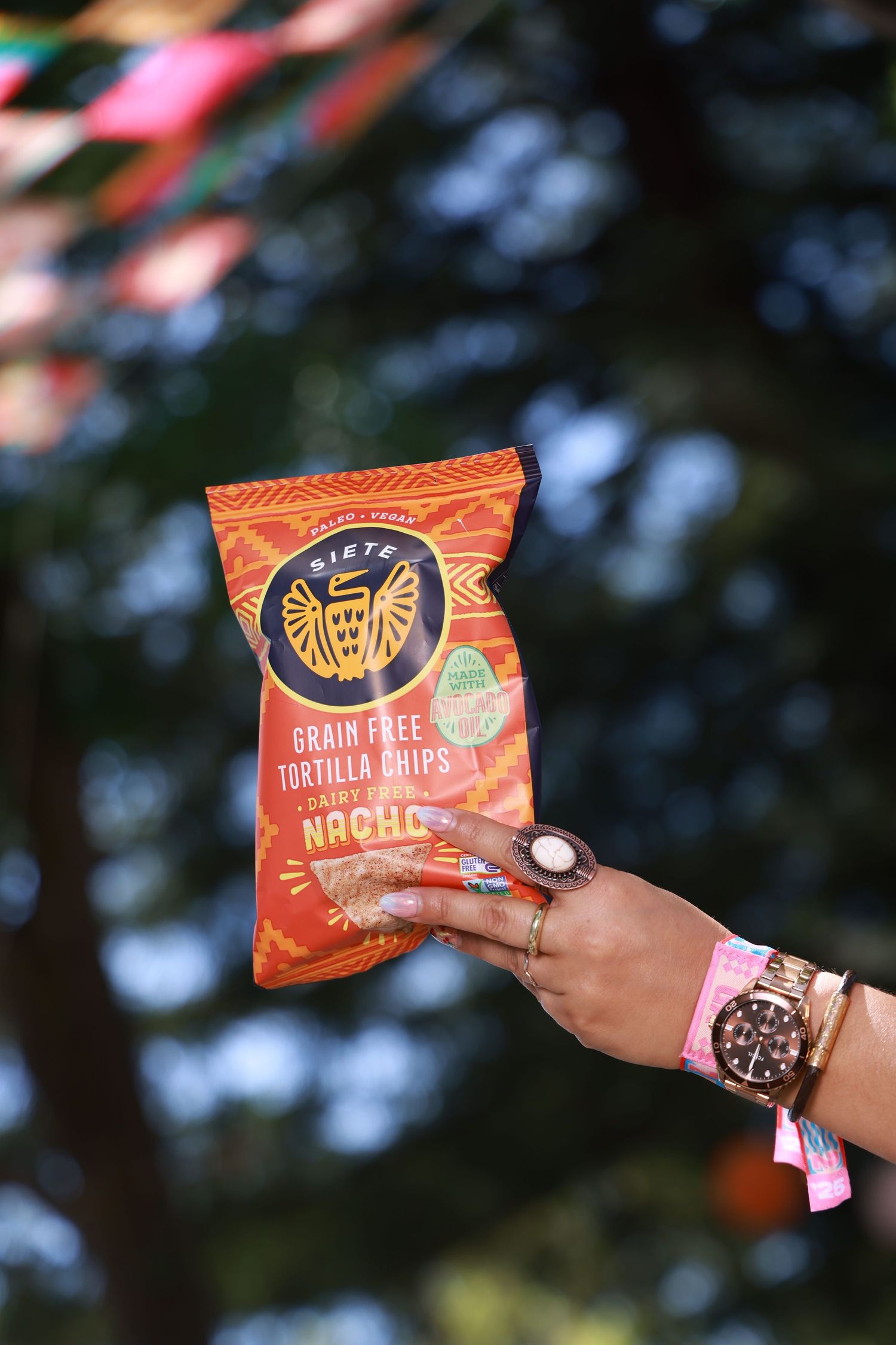 Orange tortilla chips package being held up against a blurred outdoor background.