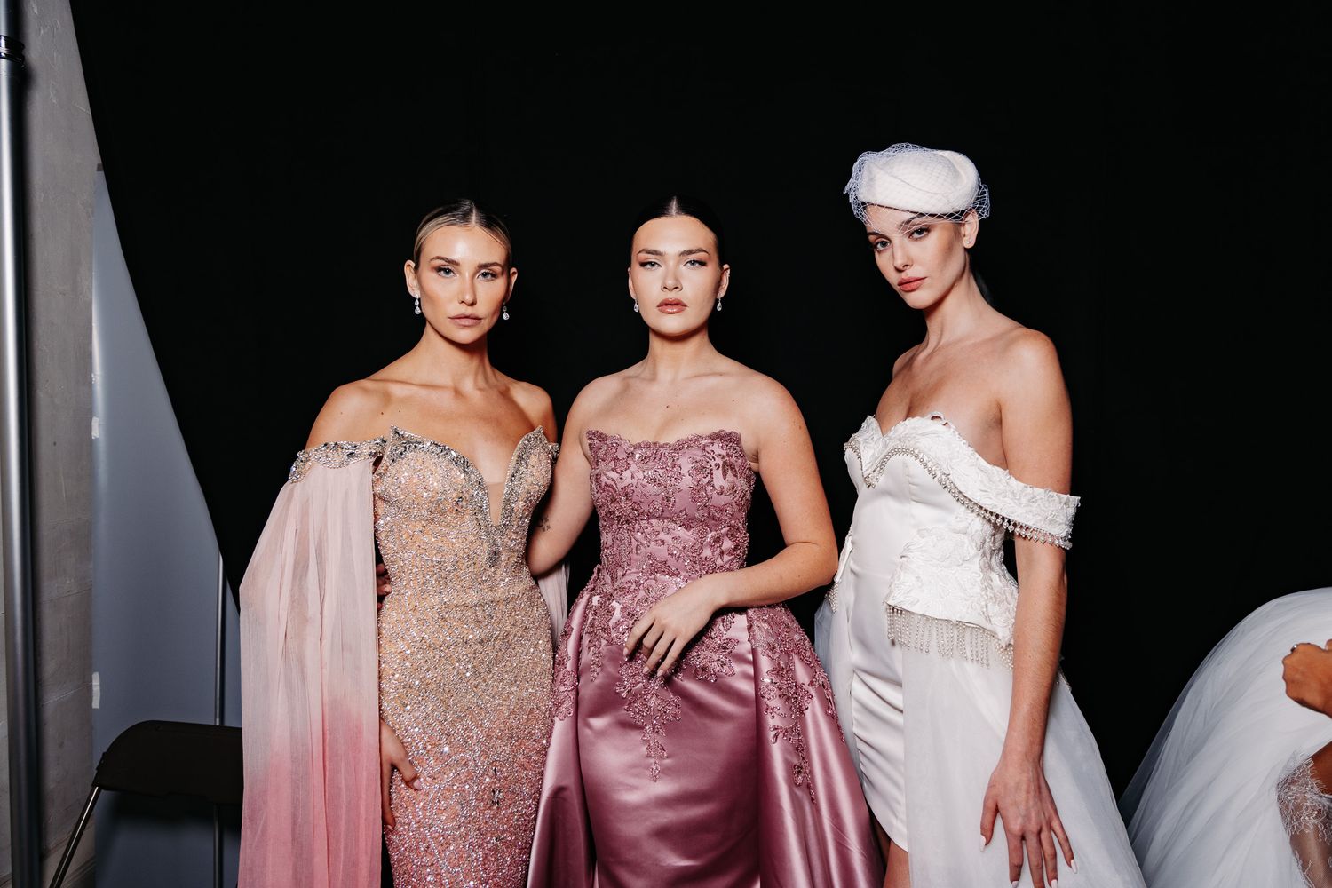 Fashion show models wearing elegant evening gowns in blush and mauve tones on dark runway.