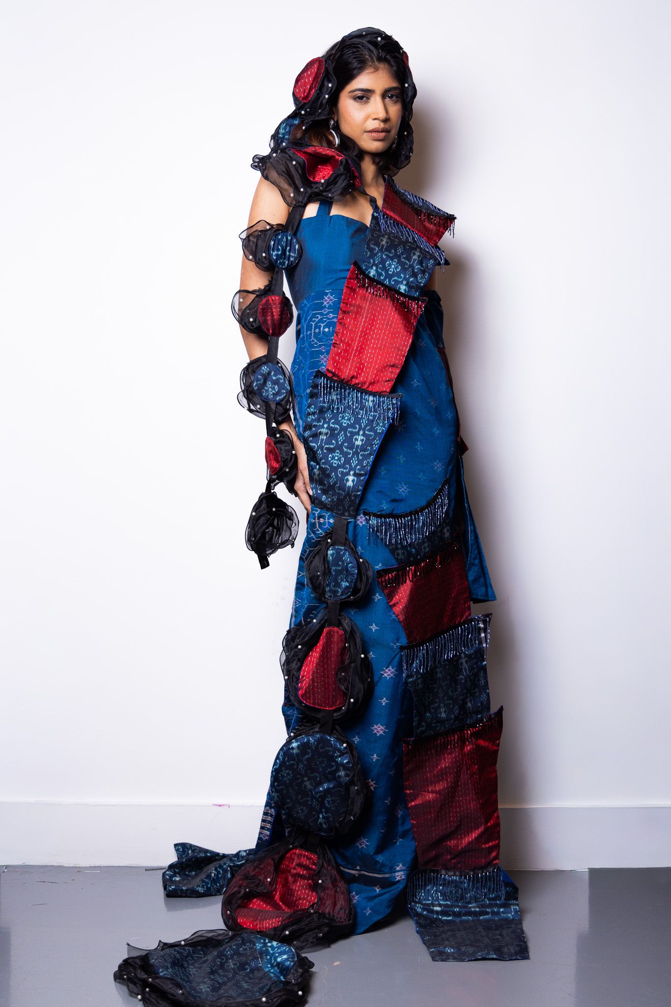Dramatic fashion pose in red and blue patchwork dress with textured fabric details.