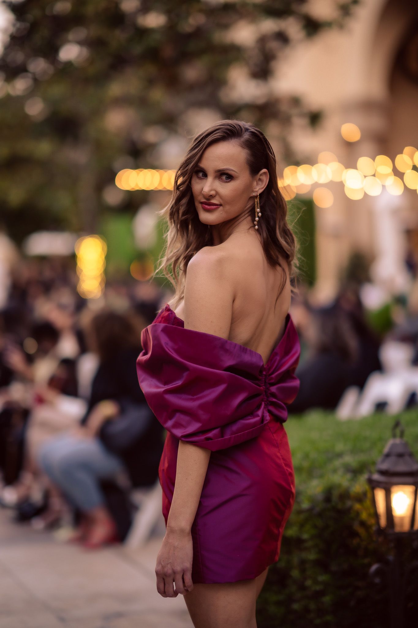 An elegant burgundy velvet evening dress captured during golden hour at an outdoor event.