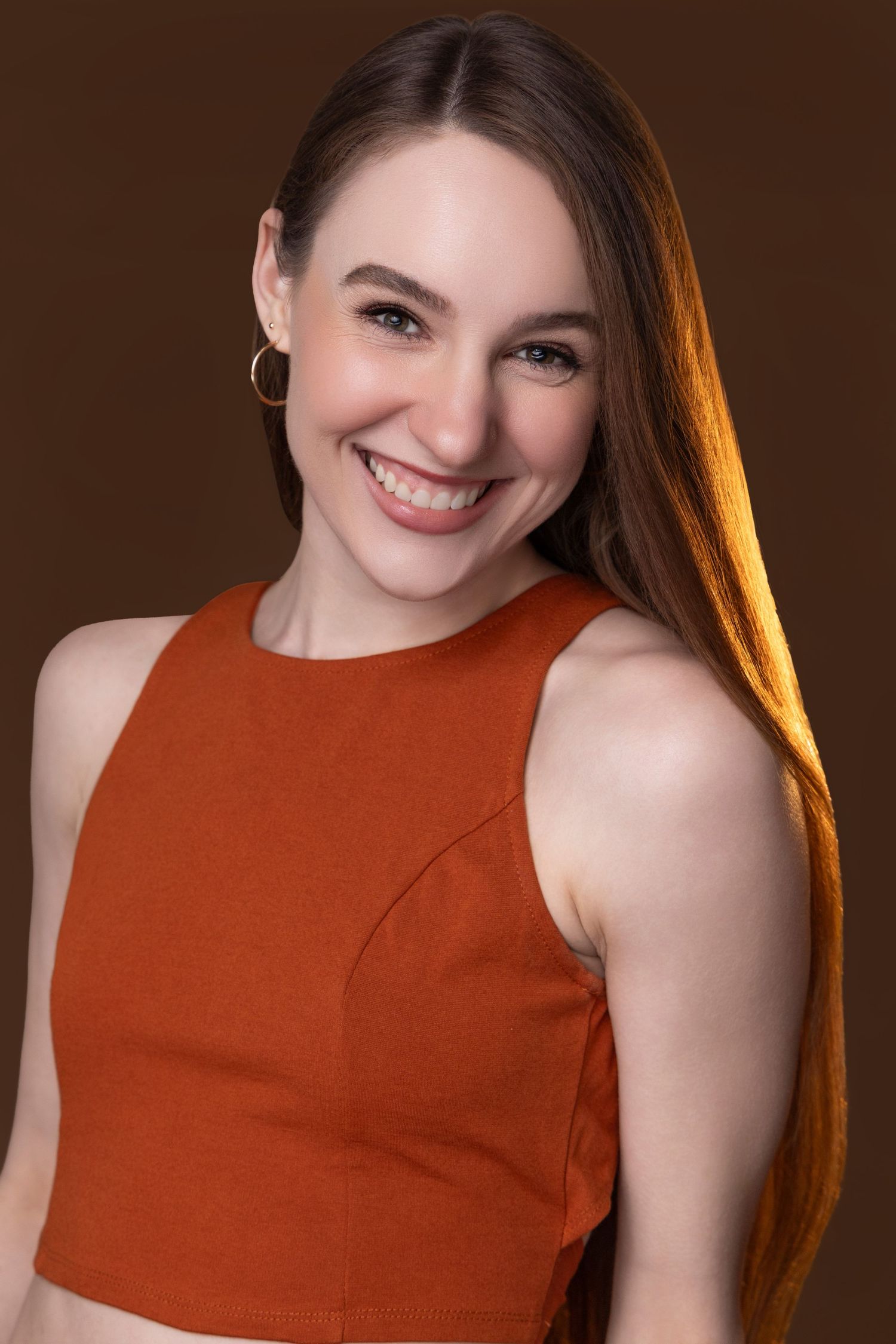 Portrait of a smiling woman wearing a rust-colored sleeveless top against a brown background.