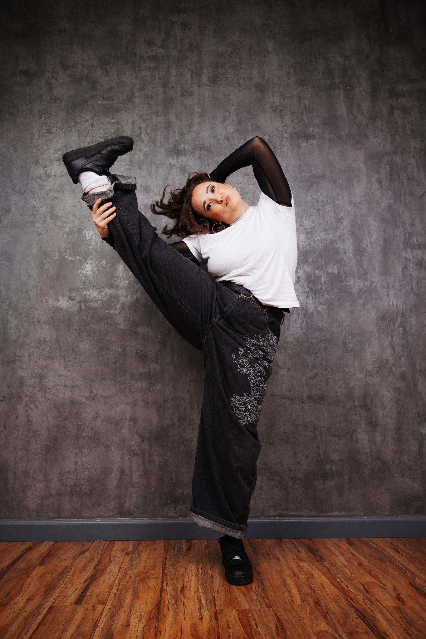 Hip hop dancer executes high-energy kicks and poses in black and white outfit against grey backdrop.