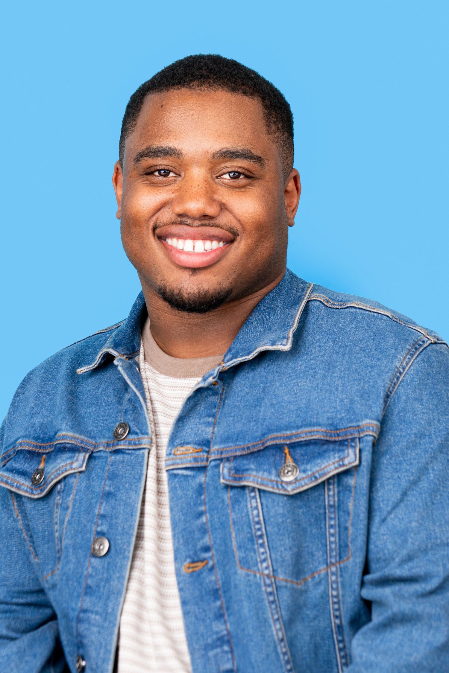 A man wearing a denim jacket and white t-shirt poses against a blue background in a photo series.