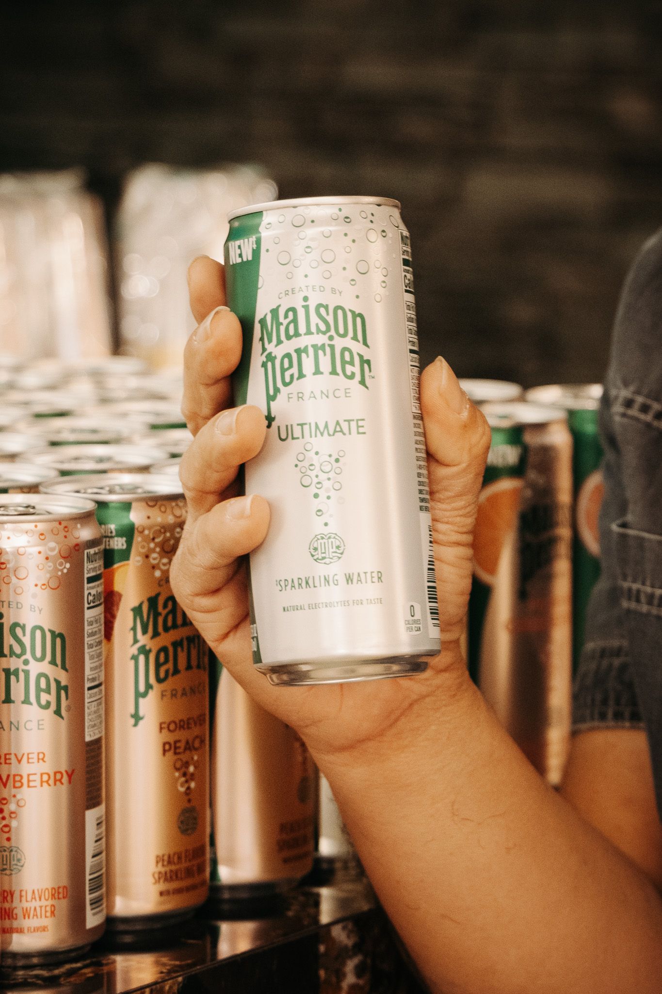 Four sequential close-up photos of hands holding cans of Maison Lillet beverage against a dark background of bottles.
