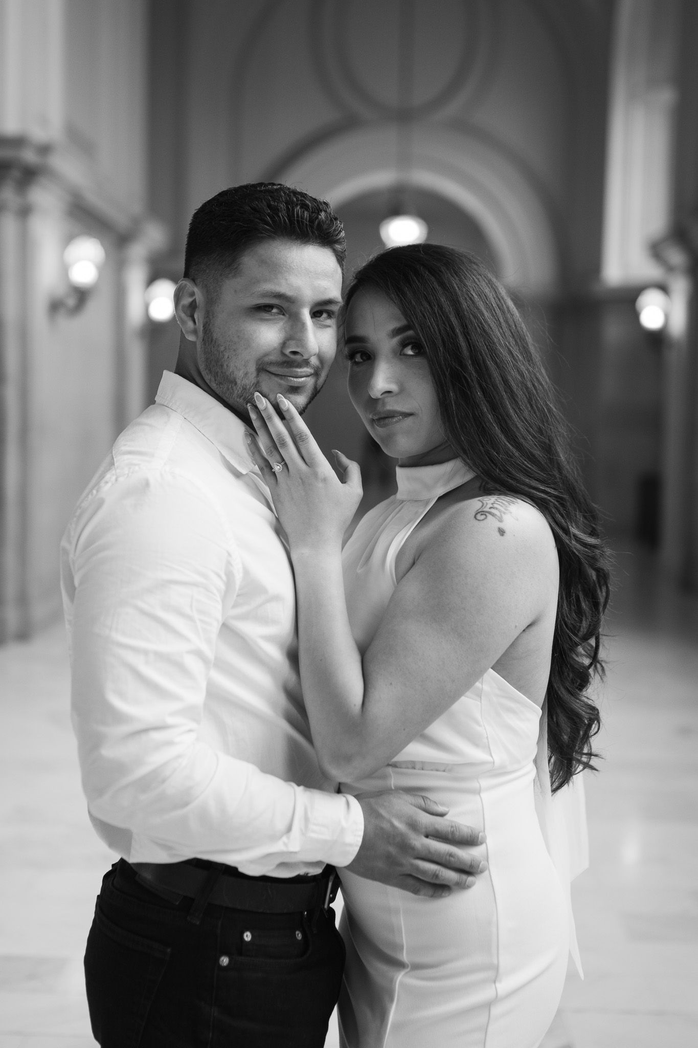 Black and white romantic portraits of a couple embracing in a grand historic building with beautiful natural lighting.