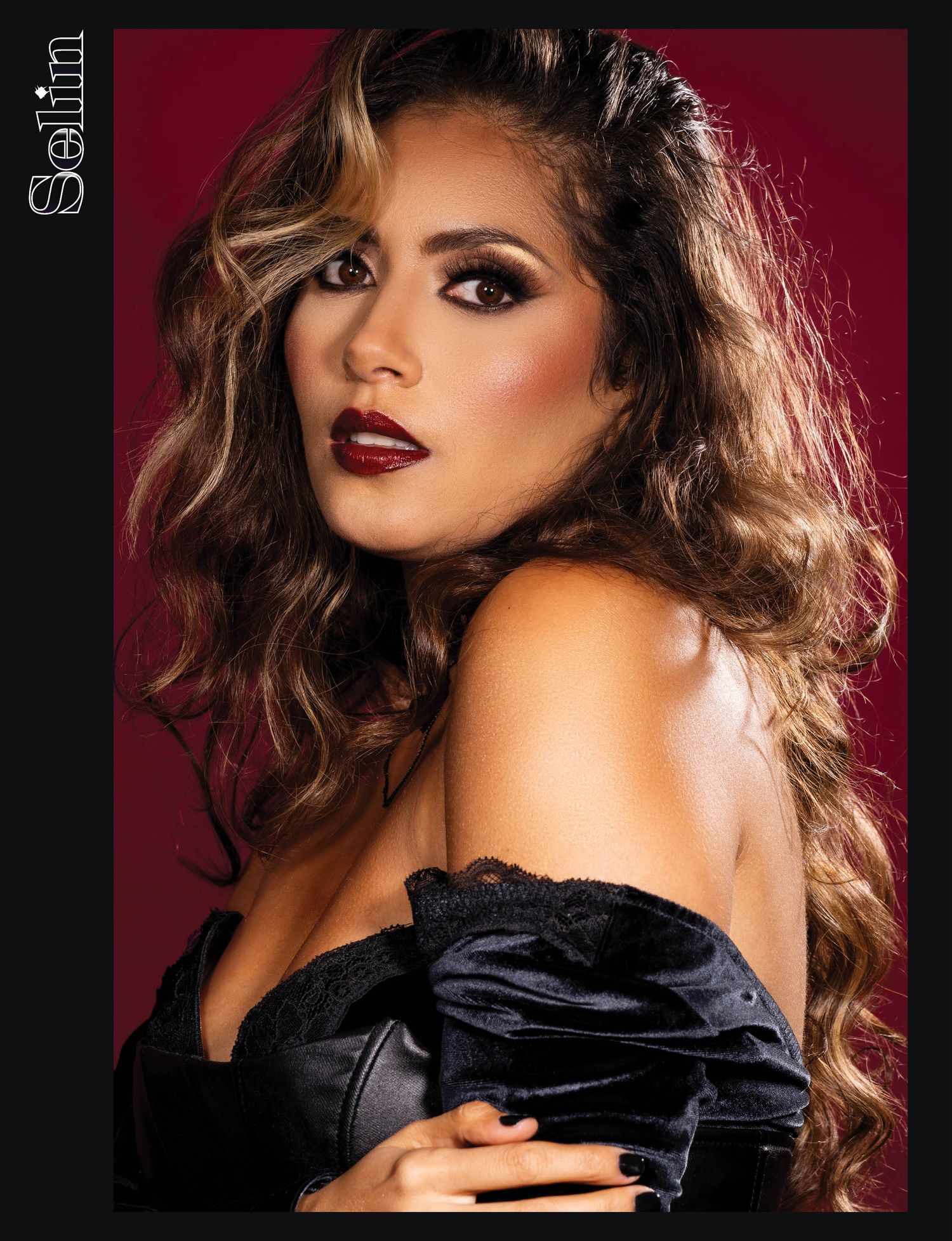 Fashion model in black attire against red backdrop showcasing glamorous makeup and wavy hair.