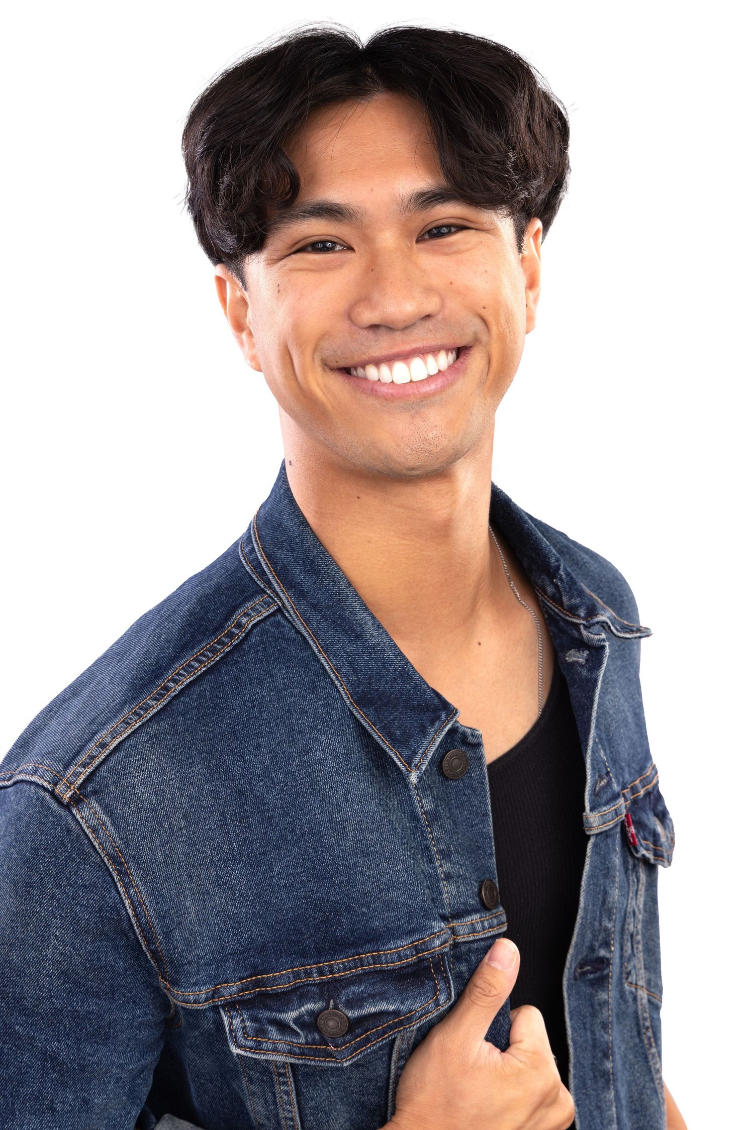Person wearing a denim jacket smiles warmly against a white background in a casual portrait series.