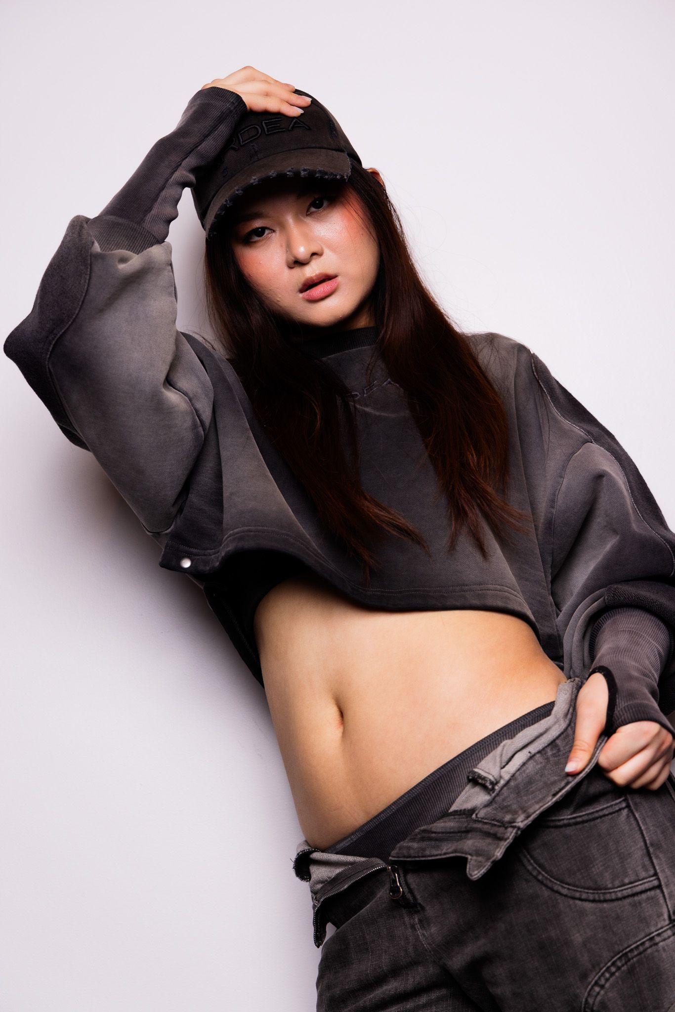 Fashion model in dark streetwear striking dynamic poses against white studio background.