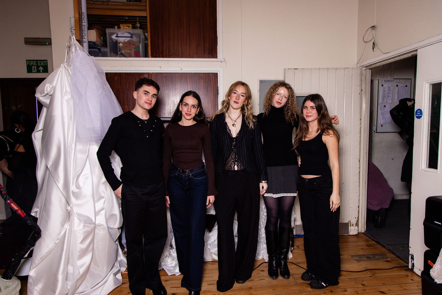 Group of people in black attire stand together in an art gallery space with white walls and hanging fabric installations.