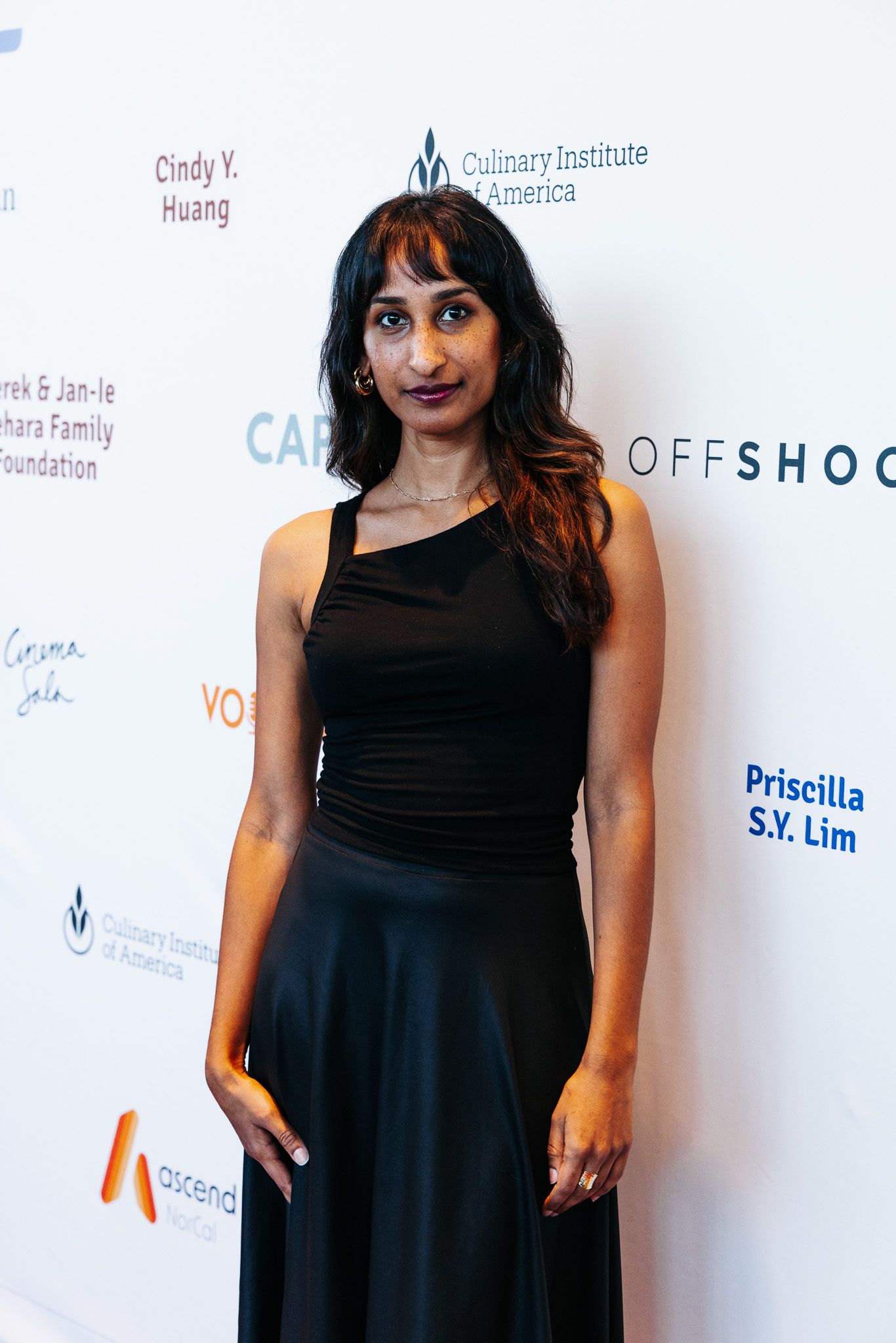 A person wearing a black dress poses against a white backdrop with film festival sponsor logos.