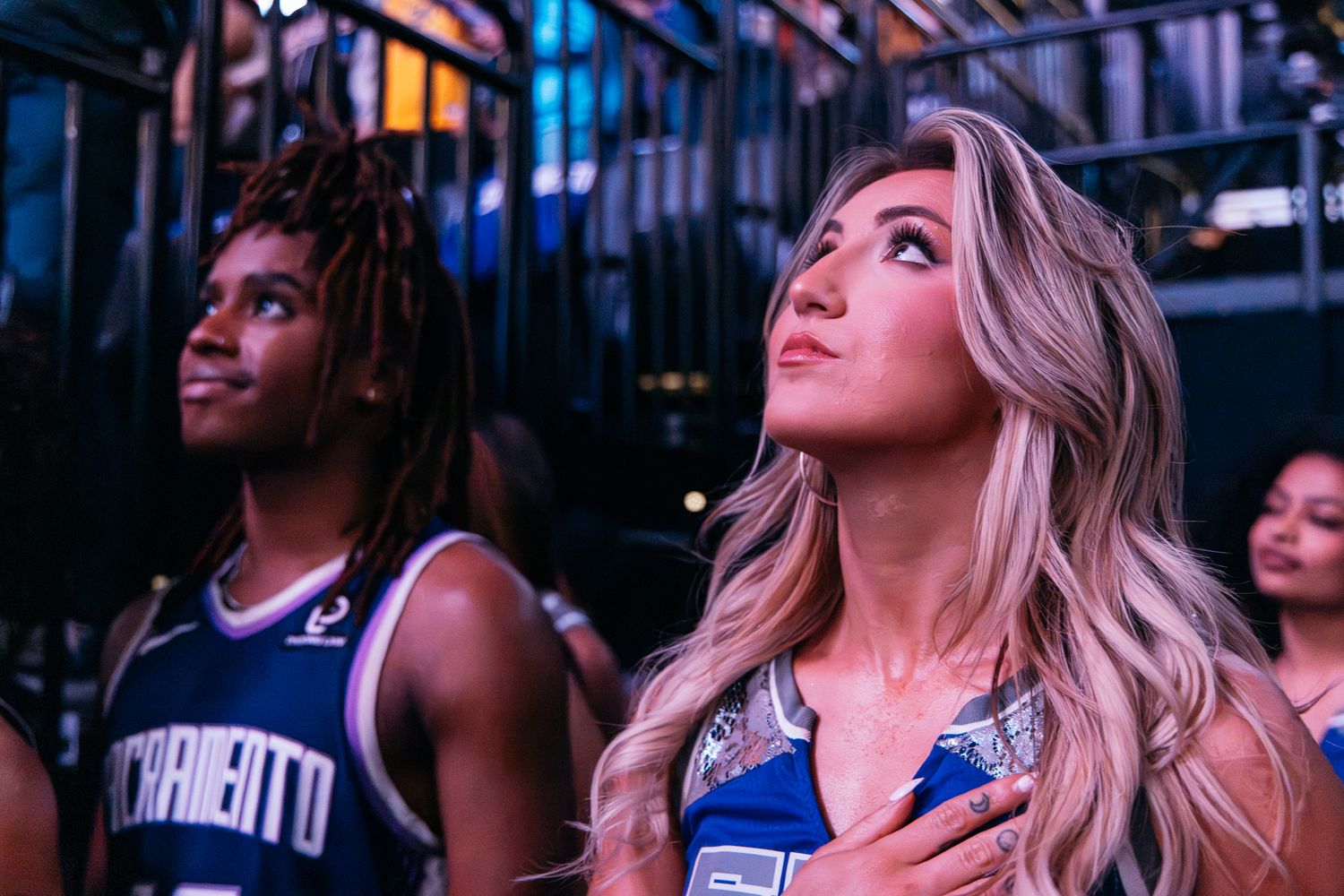 Sacramento Kings dancer and player stand attentively during national anthem at NBA arena event.