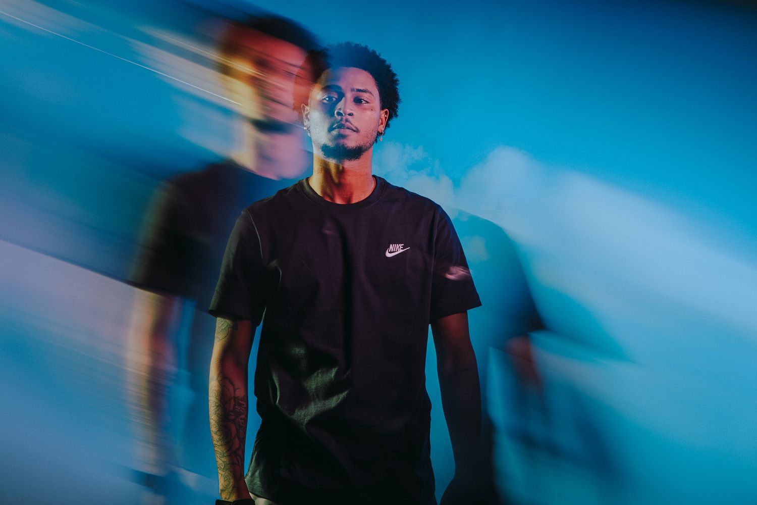 Young man in black Nike t-shirt poses with motion blur effect against blue background.