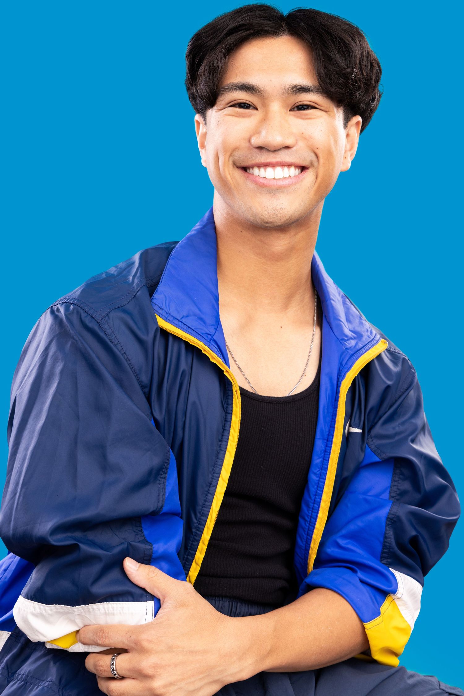 Person wearing navy and yellow windbreaker jacket poses against bright blue background with bright smile.