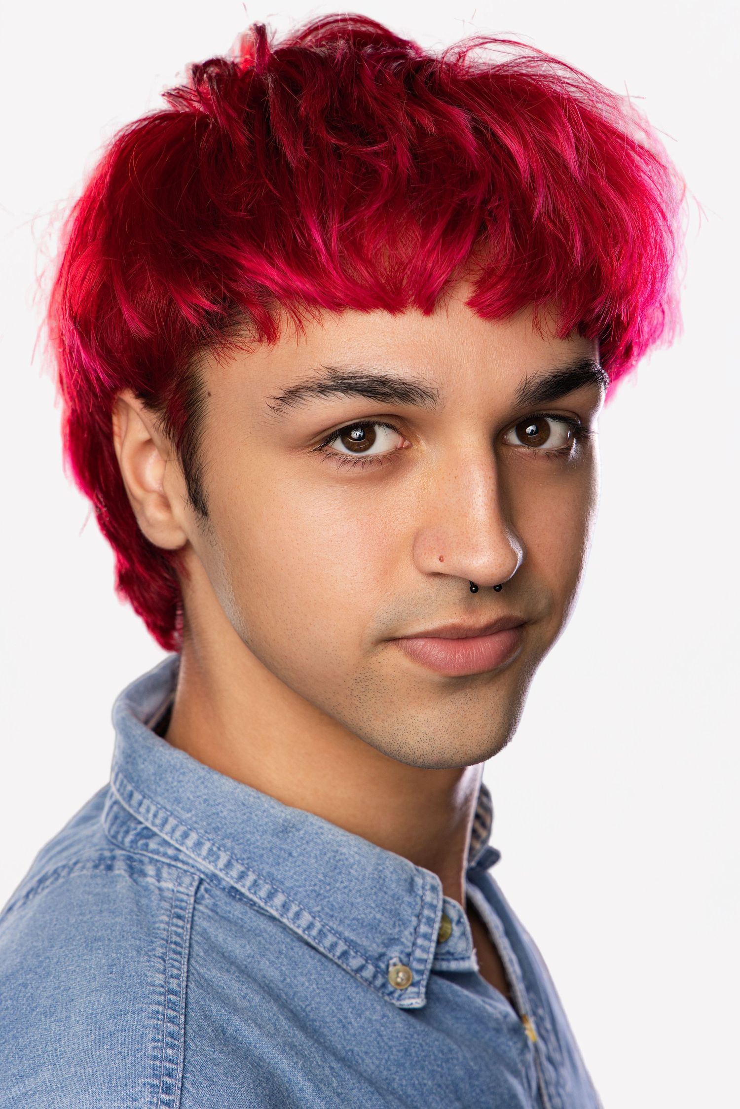 Person with bright magenta hair and nose piercing wearing denim shirt against white background in multiple poses.