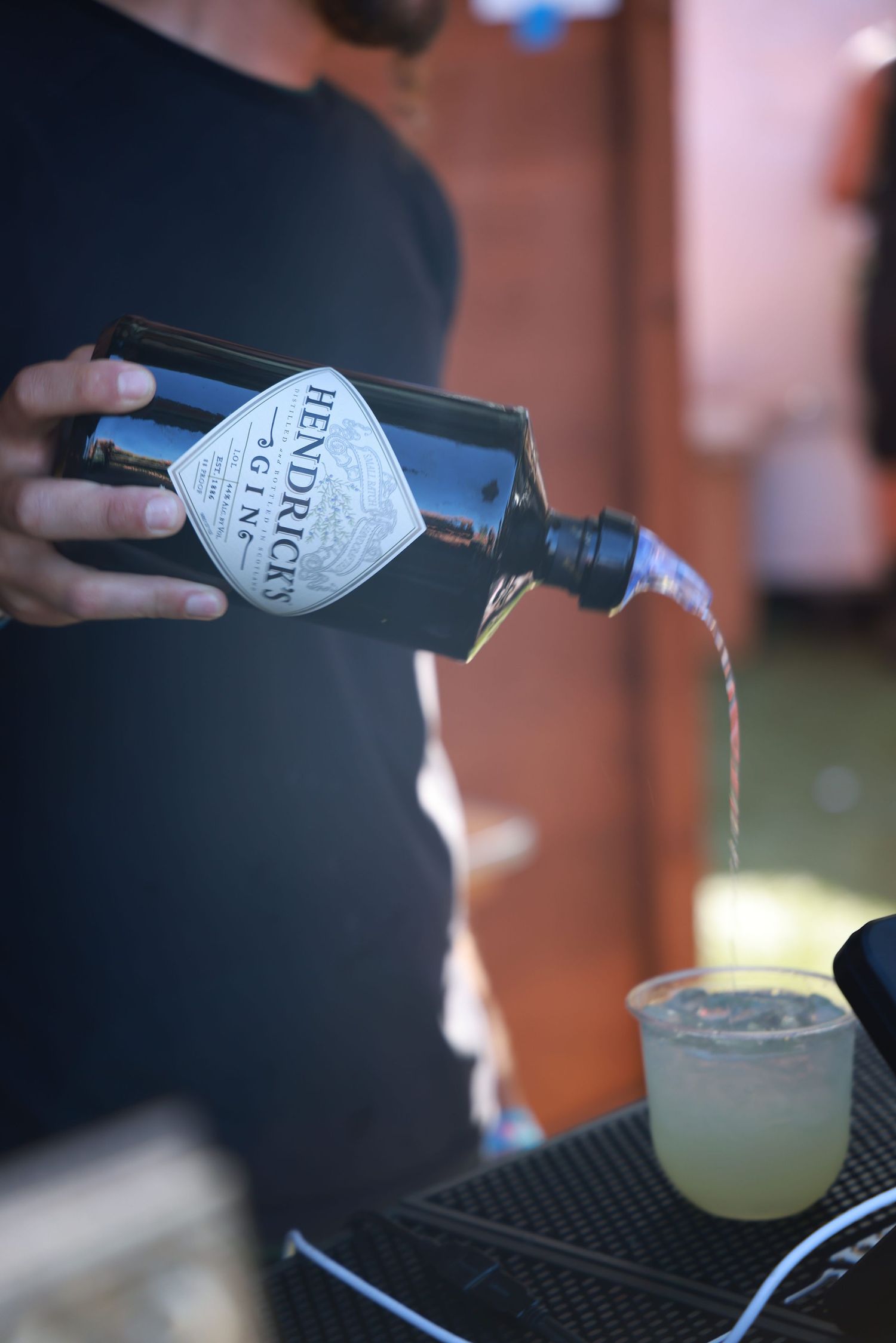 Pouring Hendricks gin into cocktail glass on black bar mat surface.