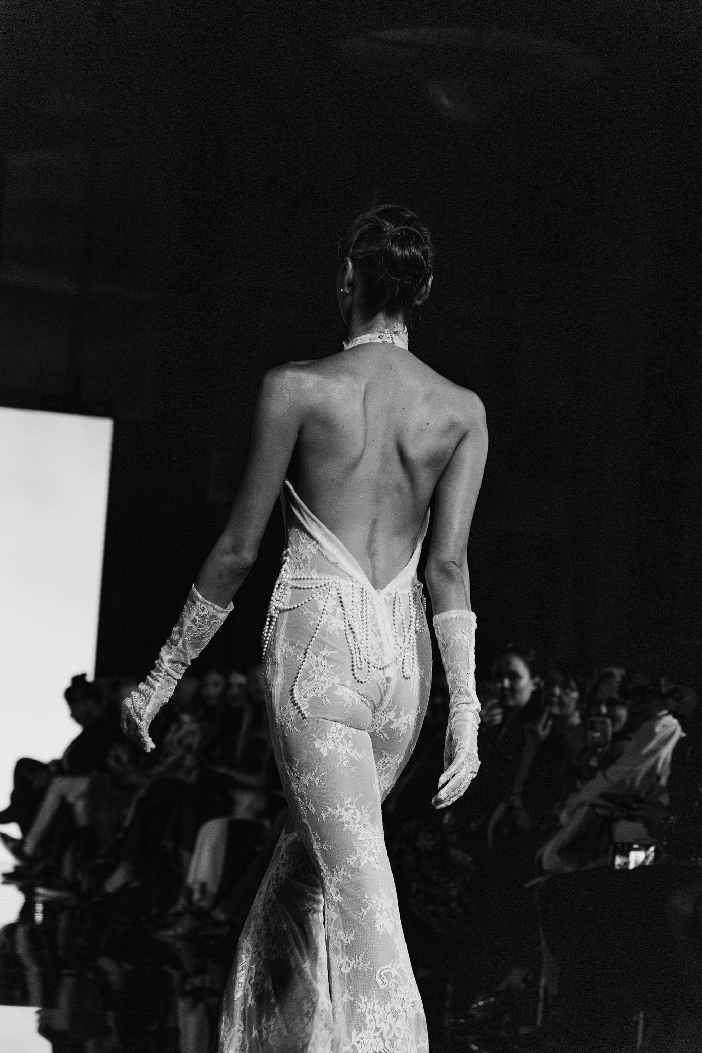 A sequence of black and white photos showing the back of an elegant wedding dress on a fashion runway.