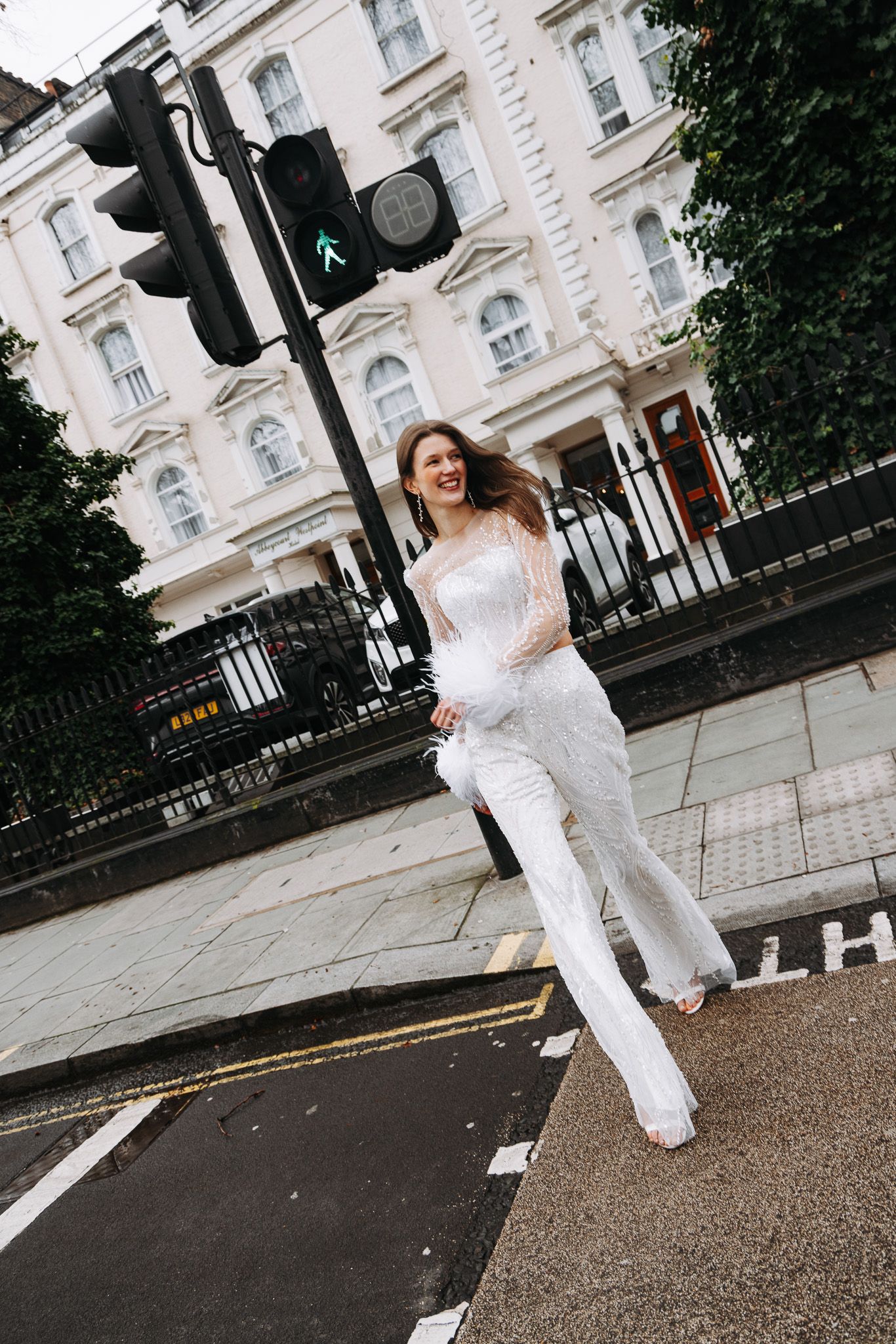 A person in a white outfit dances and jumps playfully on a London street near elegant white buildings.