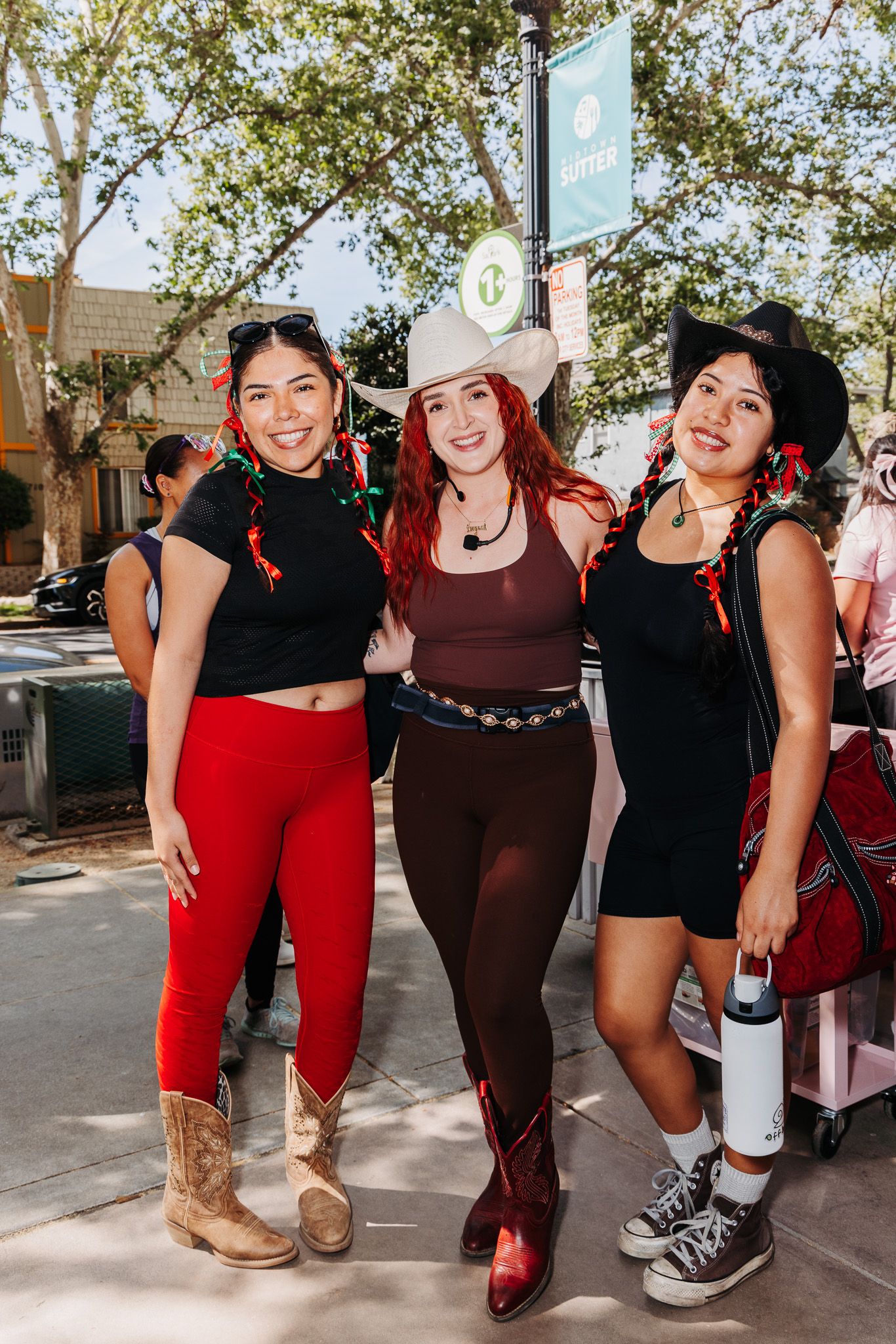 Three friends pose together at Disneyland wearing coordinated black and red outfits with western boots and casual wear.