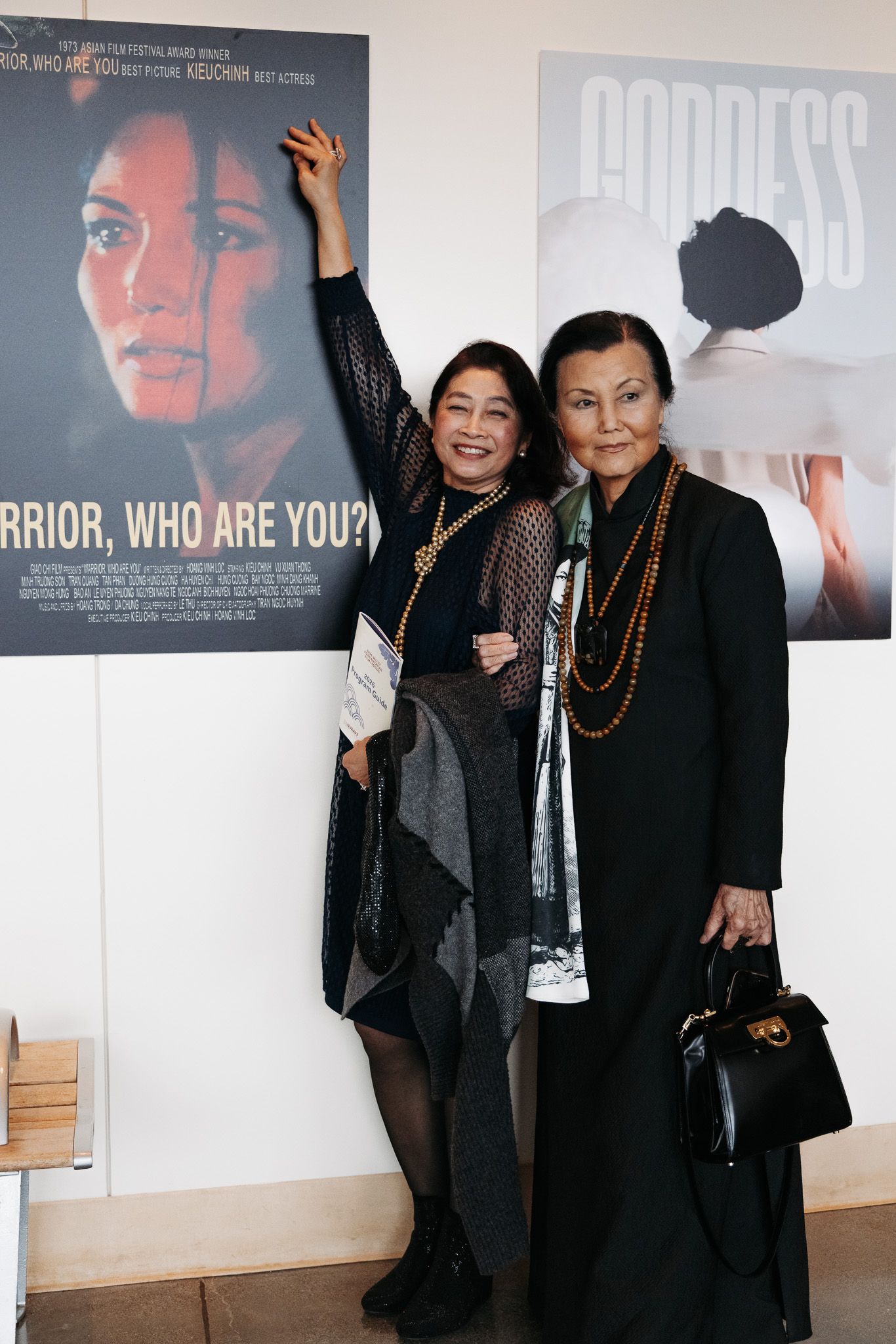 Two people pose in front of movie posters including 'Warrior, Who Are You?' at a film event.