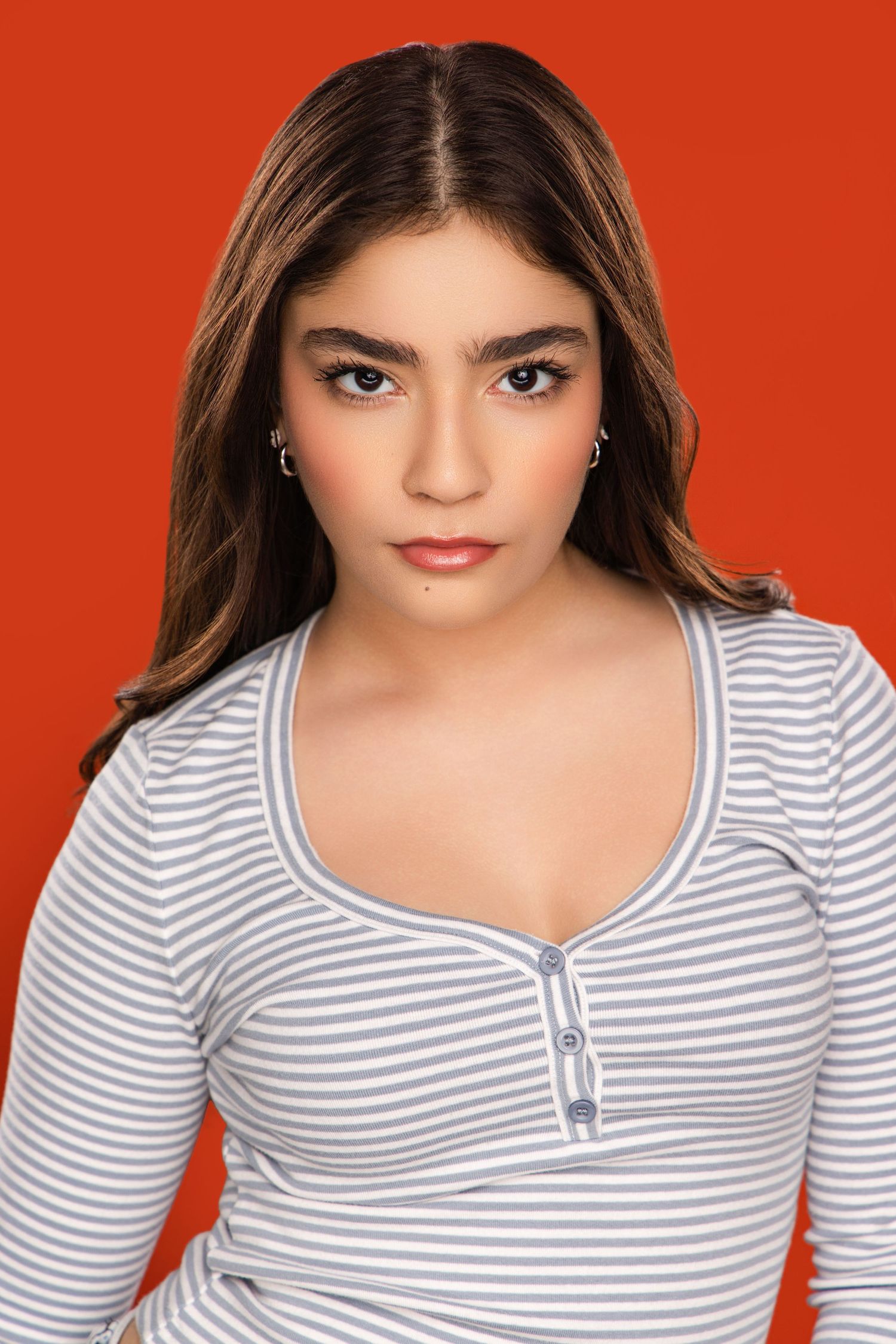 Portrait against orange background wearing striped gray and white top with natural makeup look.