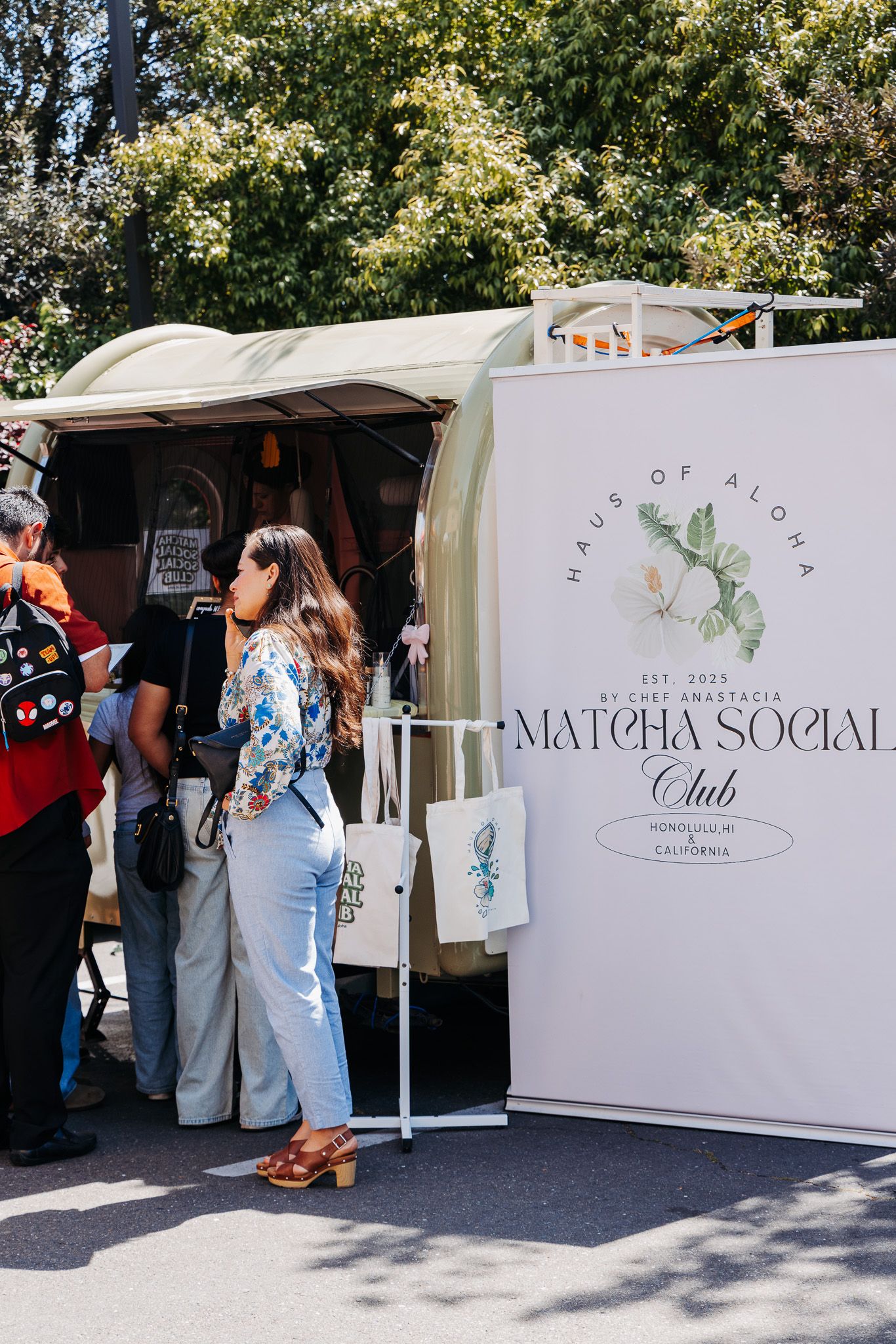 White branded event booth displays with floral accents set up at an outdoor social gathering.