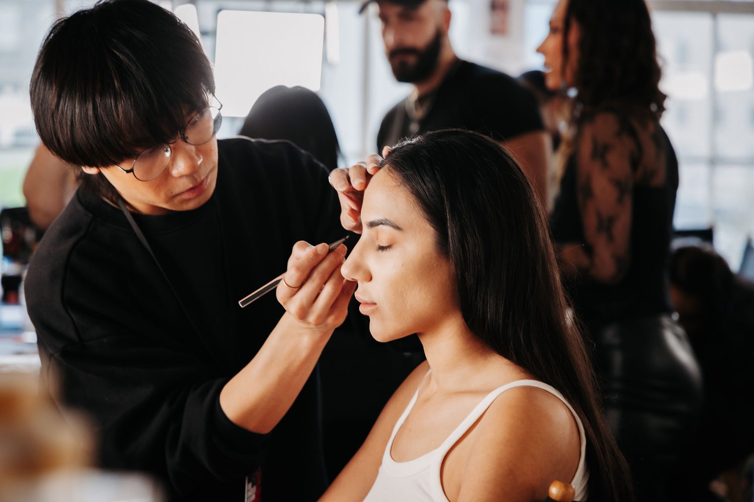 Professional makeup artist applying cosmetics to client in beauty studio with natural lighting and blurred background.