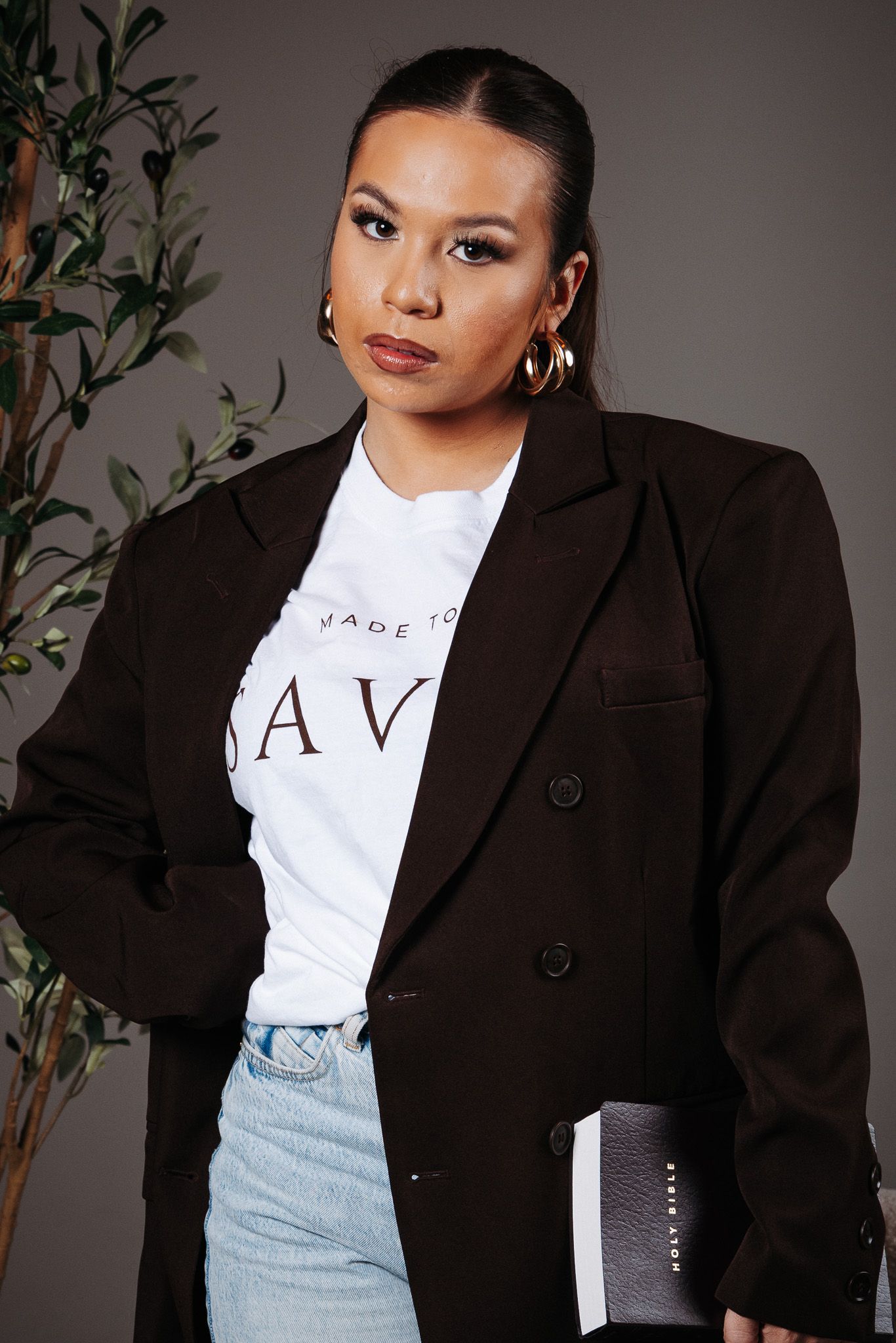 Professional model wearing a black blazer over white graphic t-shirt in studio setting with plant decor.
