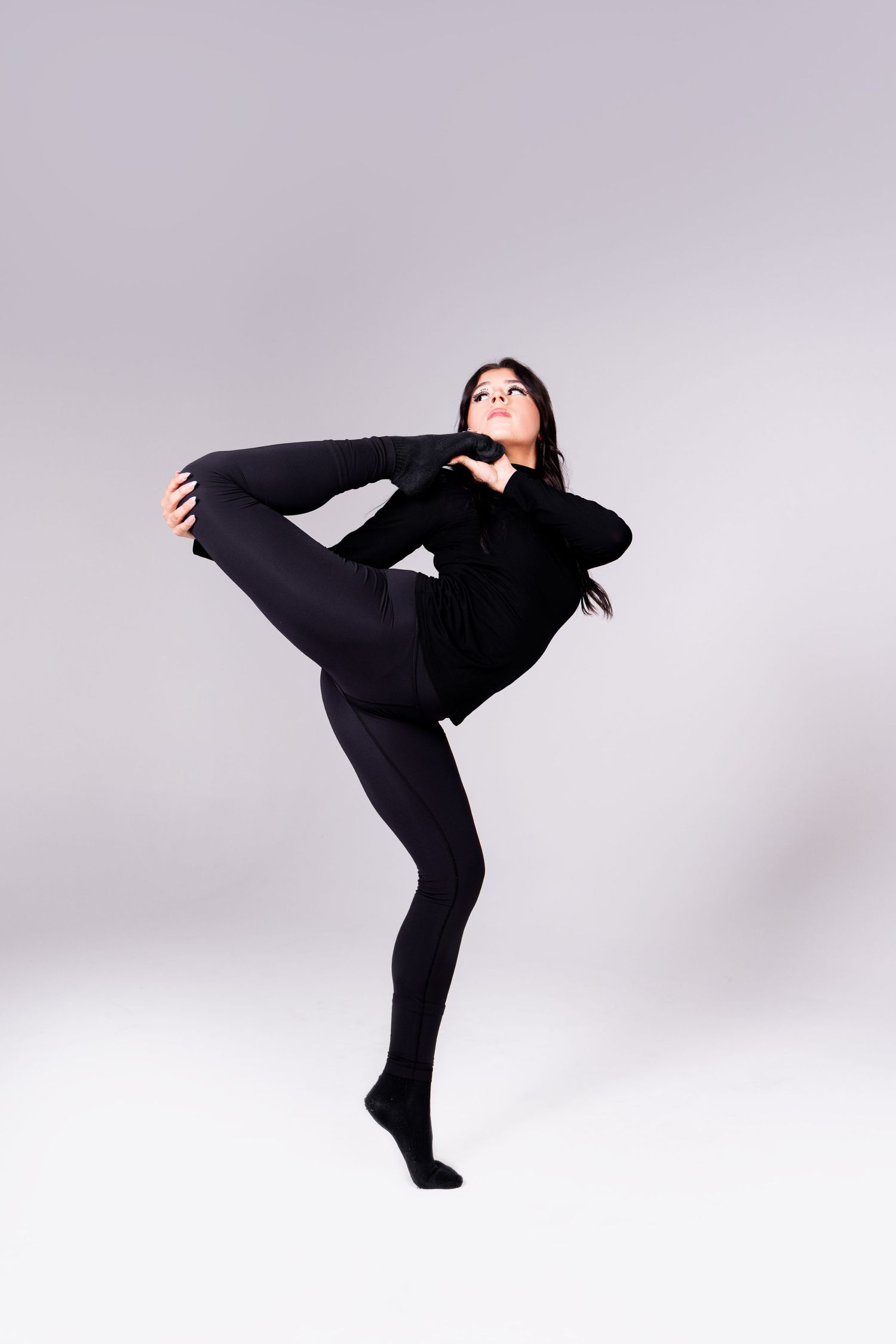 Dynamic dancer in black outfit strikes dramatic poses and movements against a light gray studio backdrop.