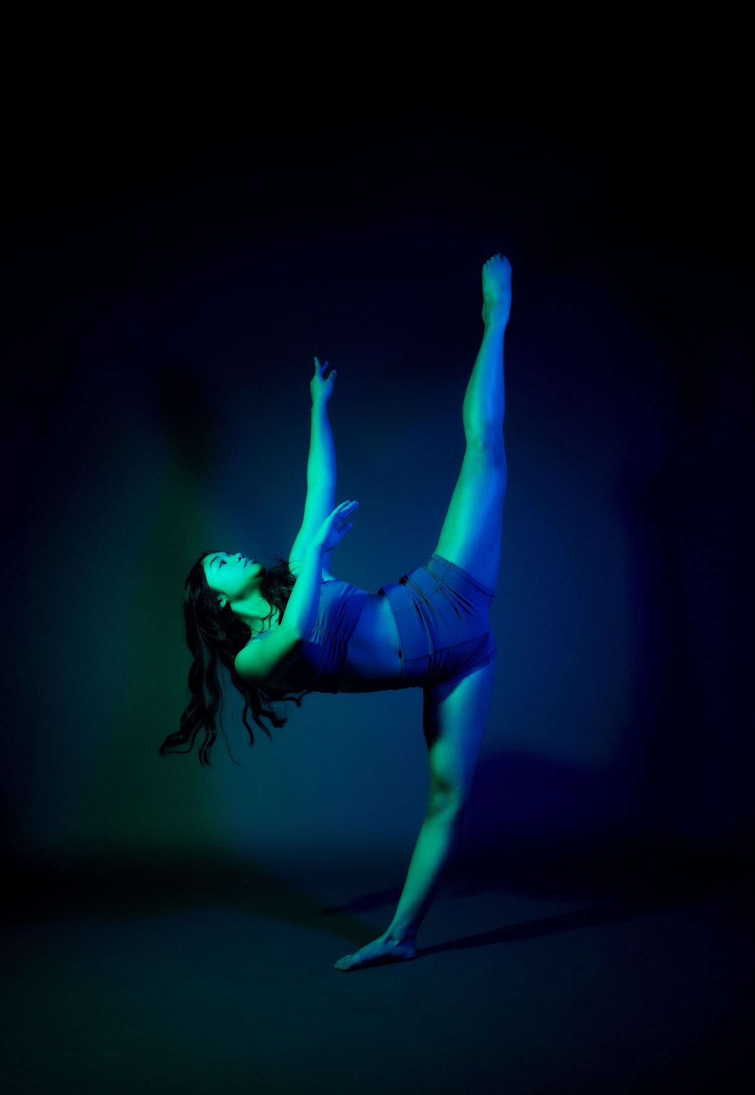 Artistic sequence showing a dancer performing aerial movements against dark background illuminated by blue and green lights.